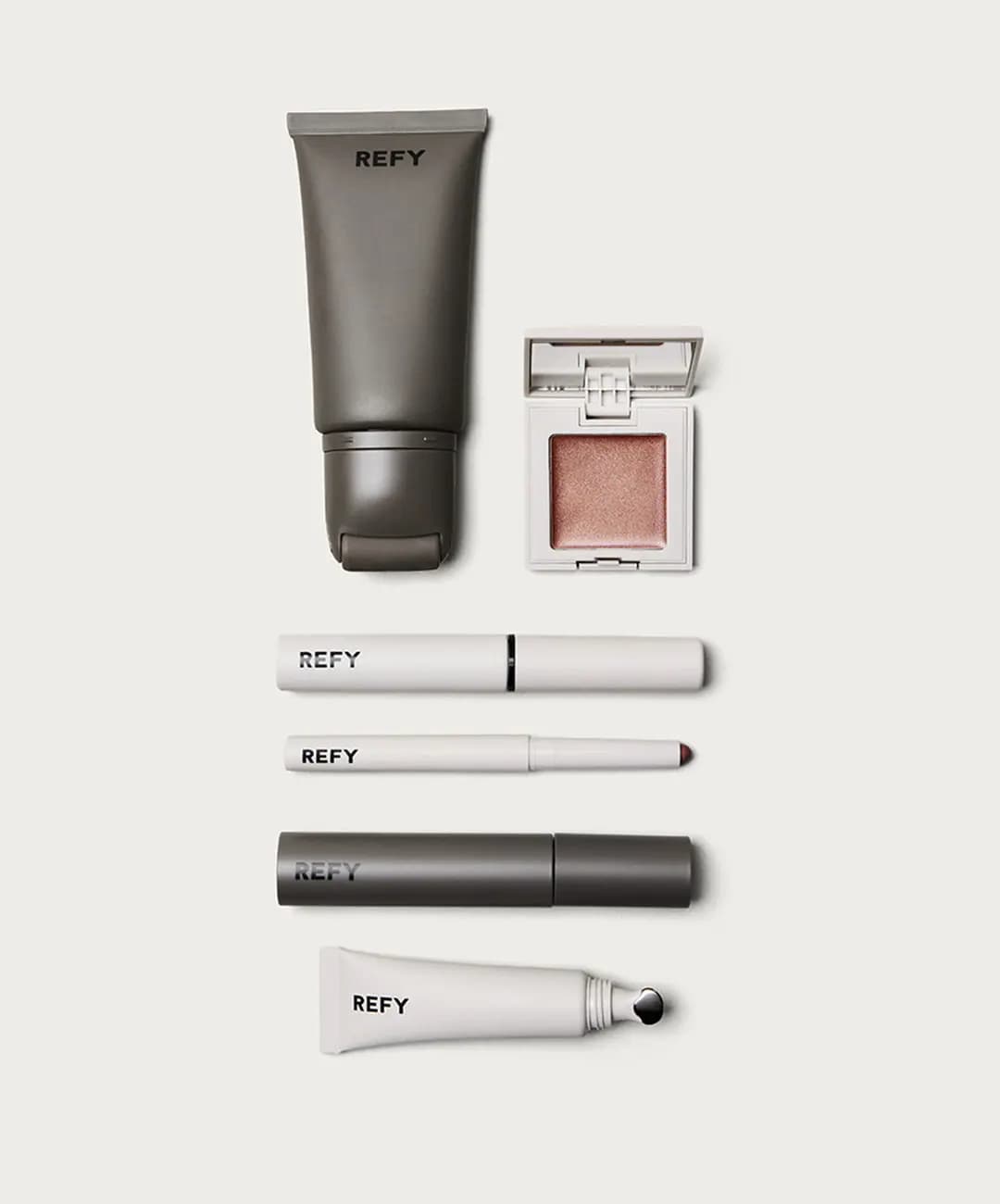 Flat lay of grey primer tube, open rose-gold cream shimmer, white tubes, lip liner, grey mascara and lip gloss tube