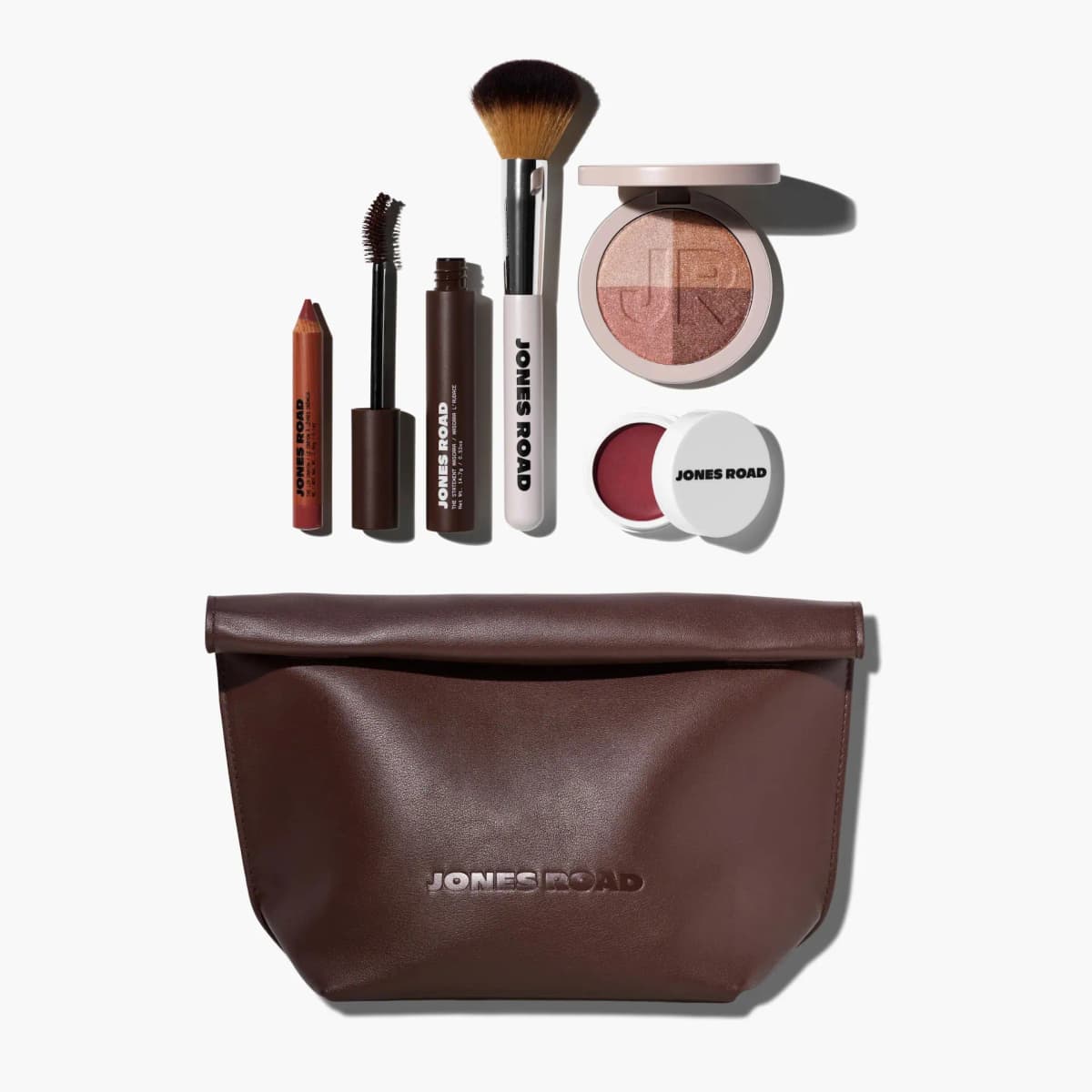Jones Road Bobbi Kit 6.0 flat lay: lip crayon, mascara, brush, four-shade highlighter, berry balm and brown leather clutch