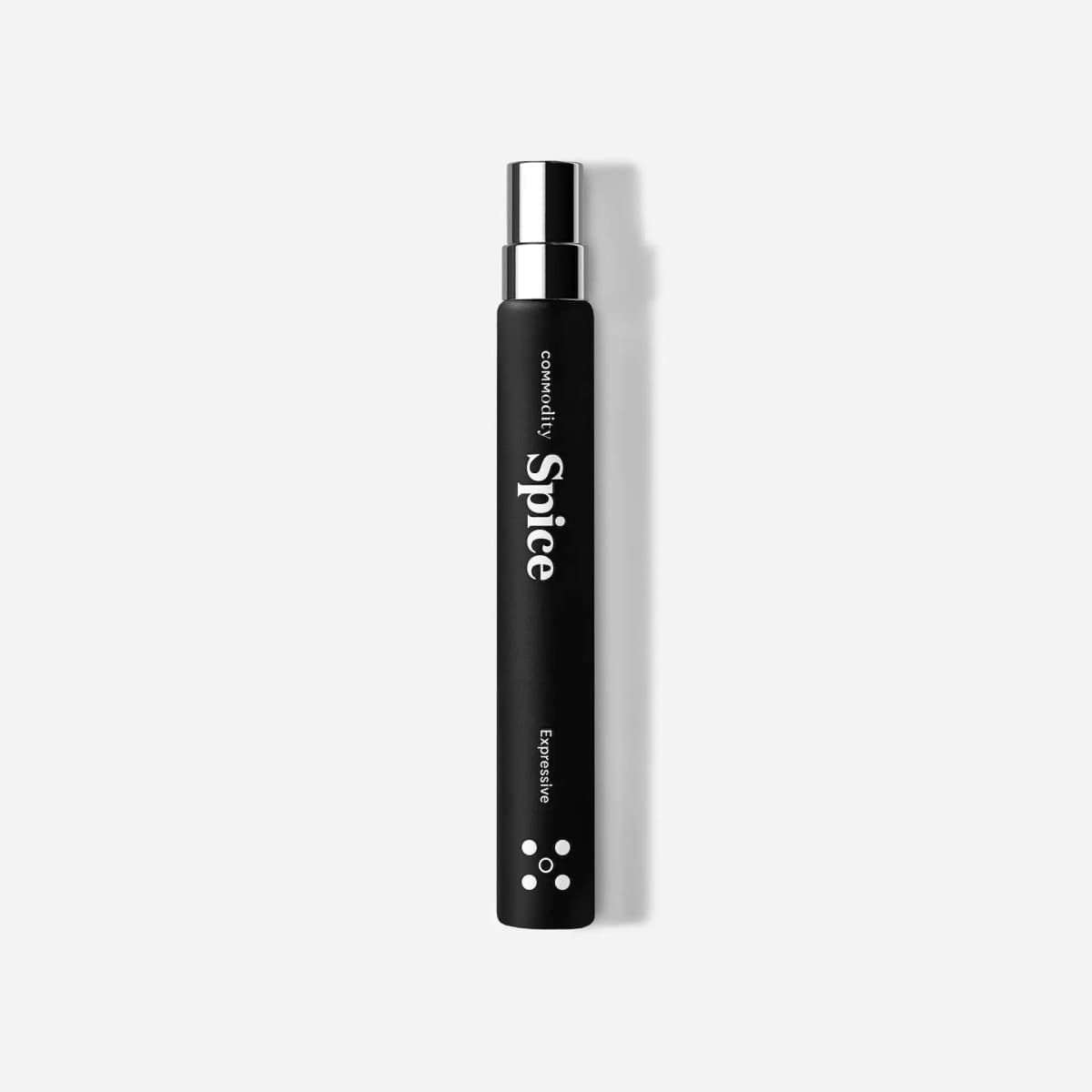 Slim matte black Commodity Spice Expressive travel spray with silver cap and dot icon, on a light grey background
