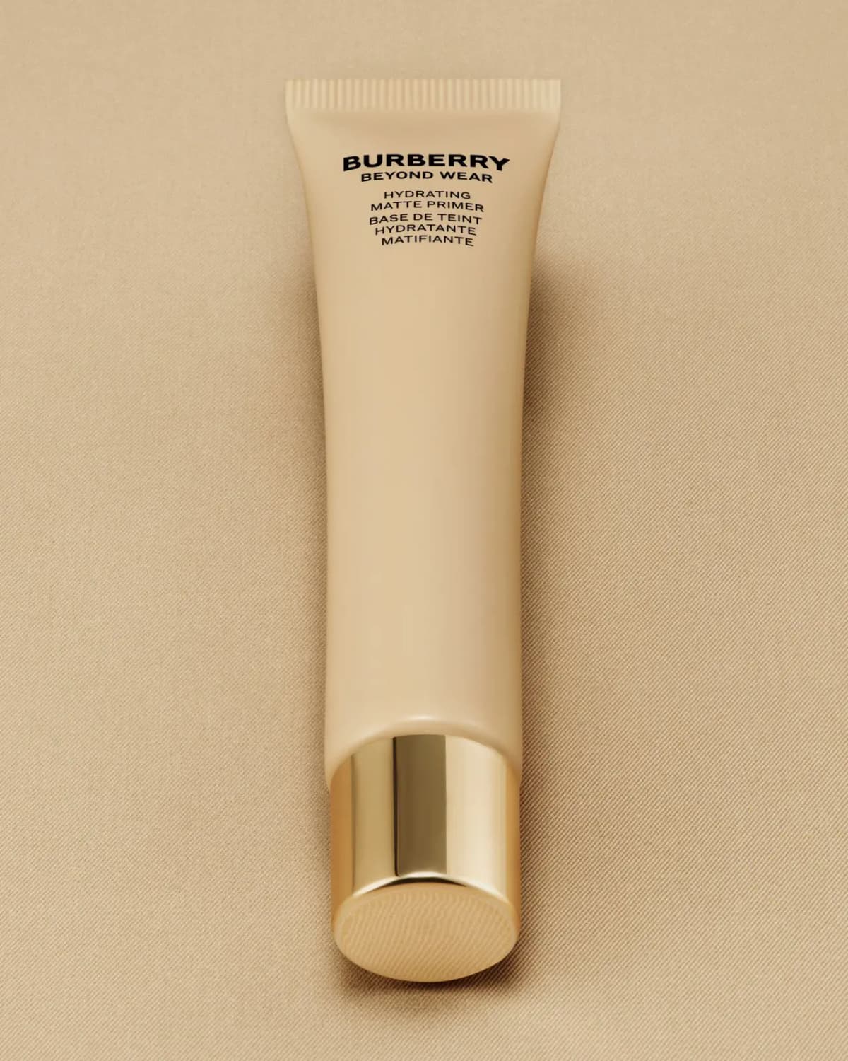Burberry Beyond Wear Hydrating Matte Primer tube laid flat on beige fabric with gold cap facing down