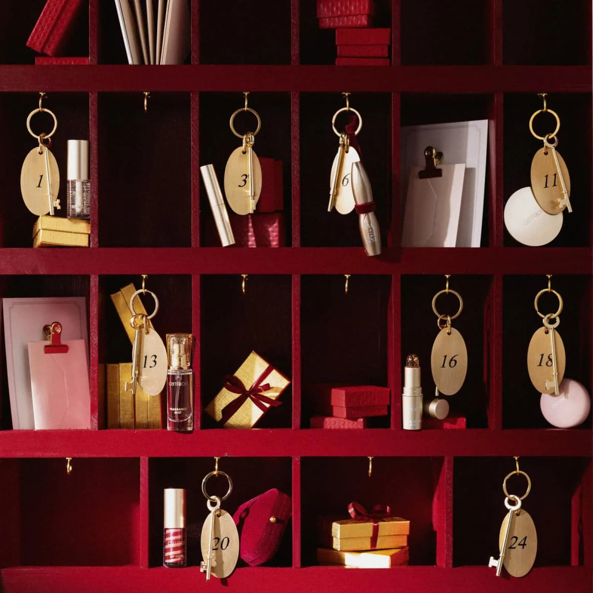 Red pigeonhole shelves with gold numbered key fobs beside Catrice lip gloss, mascara, fragrance mist and lip mask