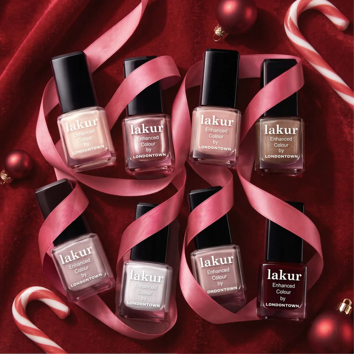 Eight lakur bottles in nudes, shimmers, white and merlot wrapped in pink satin ribbon on red velvet