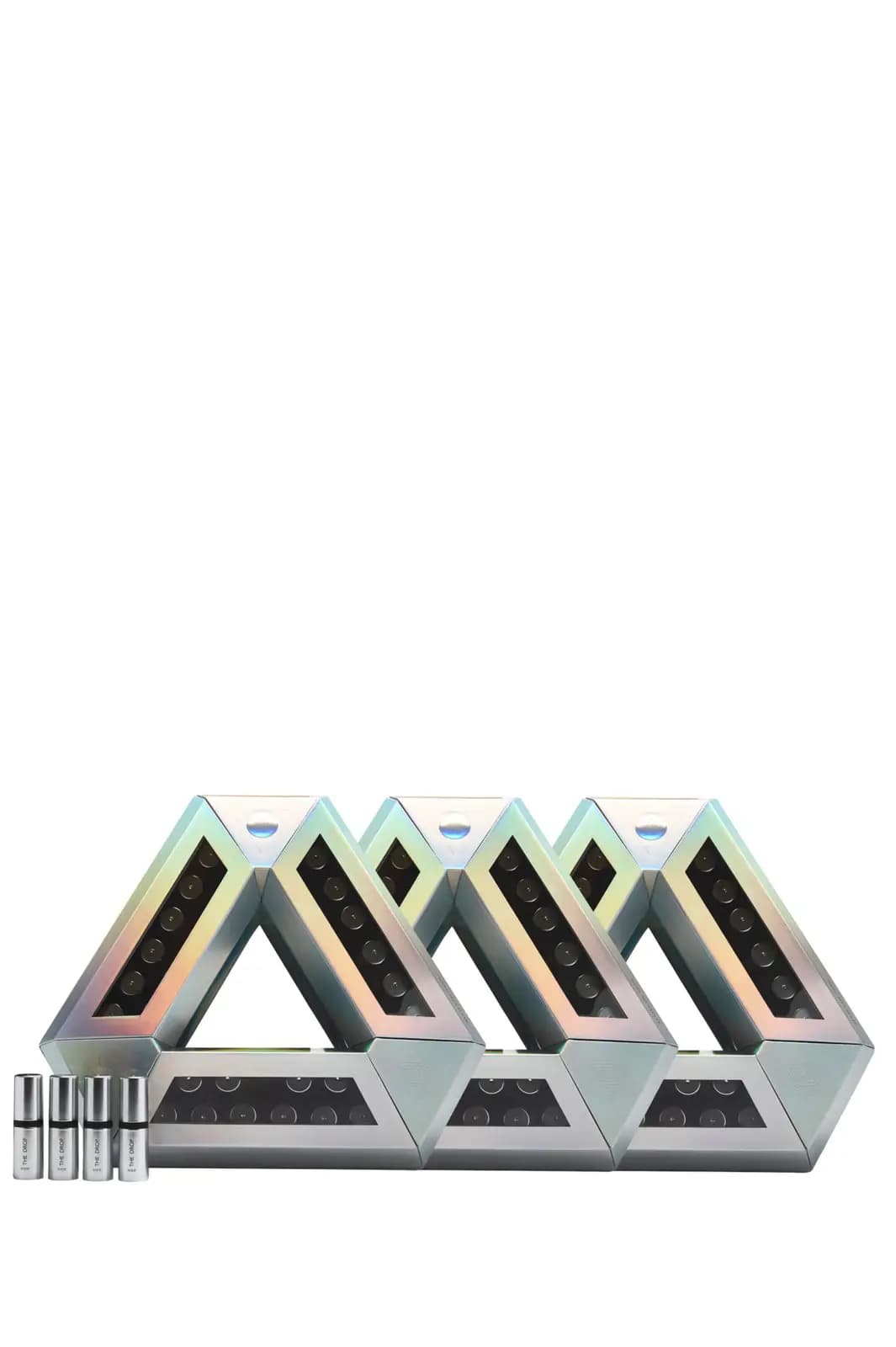Three holographic triangle cases lined up with four silver The Drop ampoules on a white background