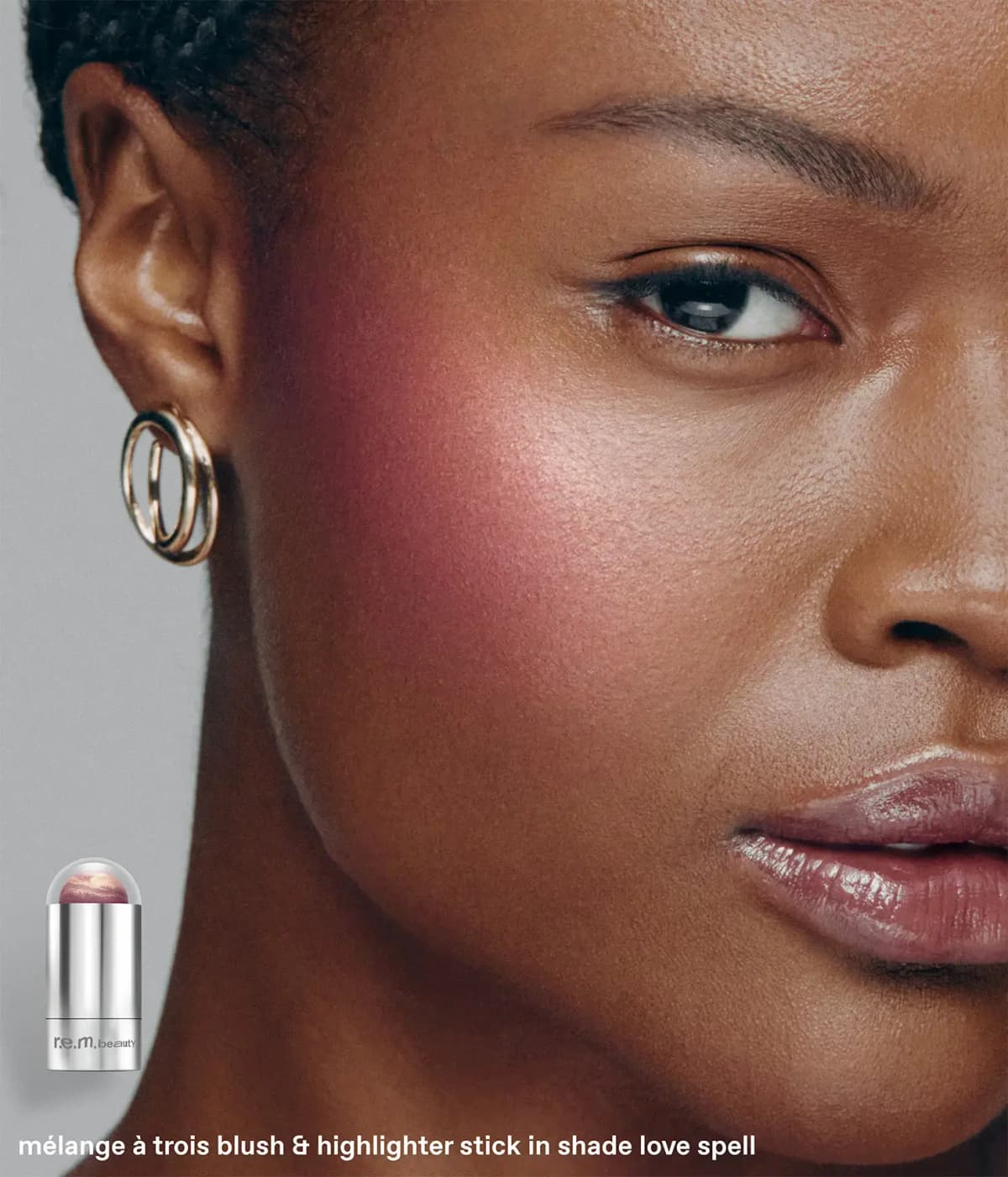 Model with deep skin wearing berry blush with pearly highlight on cheek, dome-capped silver stick inset
