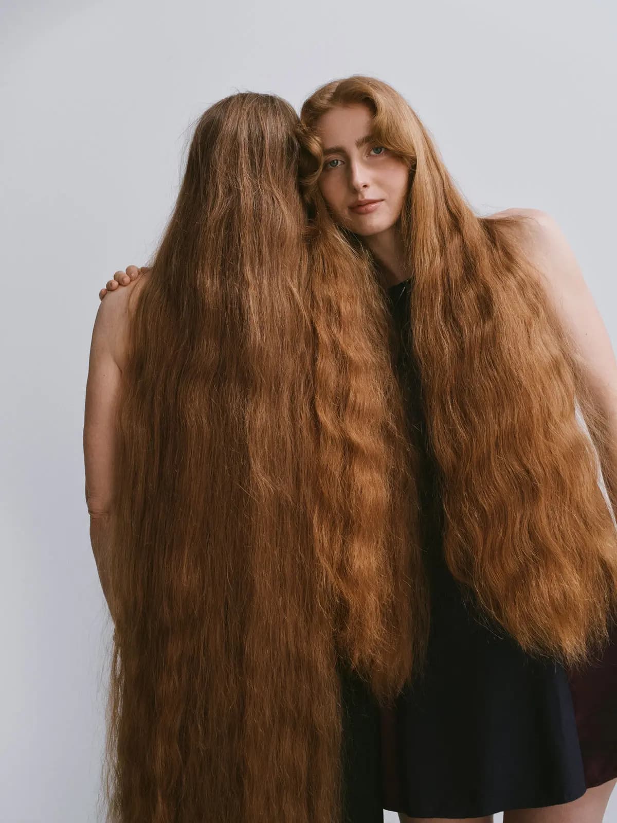 Two people embracing, one with face hidden by long wavy copper hair, the other gazing at camera with matching red hair