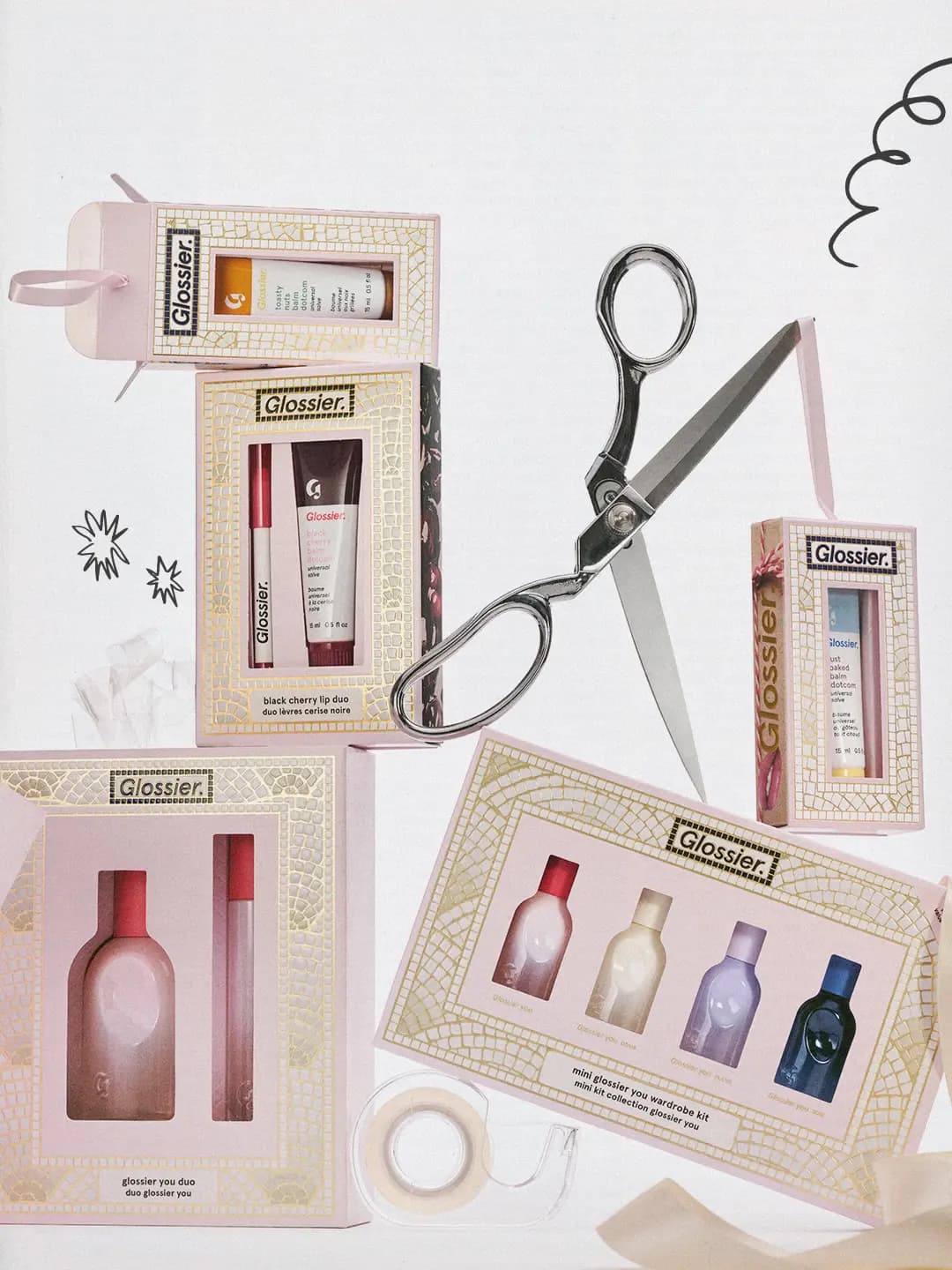 Glossier holiday gift boxes in pink mosaic packaging stacked with silver scissors, tape and ribbon