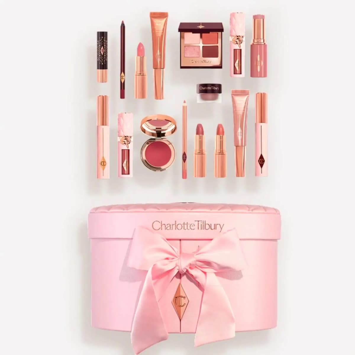 Overhead flat lay of 16 pink and rose-gold Pillow Talk makeup products arranged above a quilted pink Charlotte Tilbury