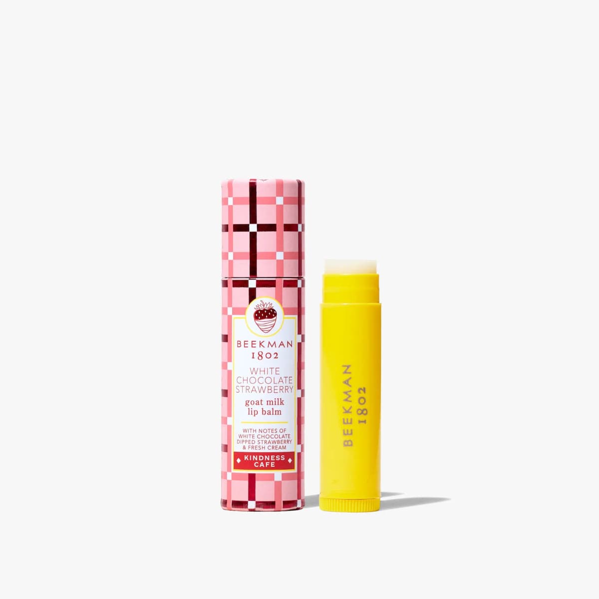 Beekman 1802 White Chocolate Strawberry goat milk lip balm in pink plaid tube beside its yellow balm stick