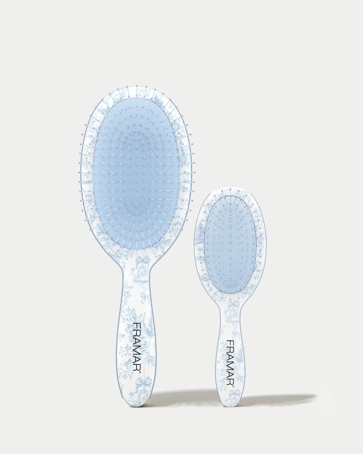 Full-size and mini FRAMAR detangling brushes with light-blue cushions and toile handles on a grey backdrop