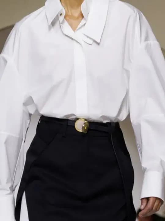 Close-up of a white oversized shirt and black skirt cinched with a slim belt and small gold compact buckle