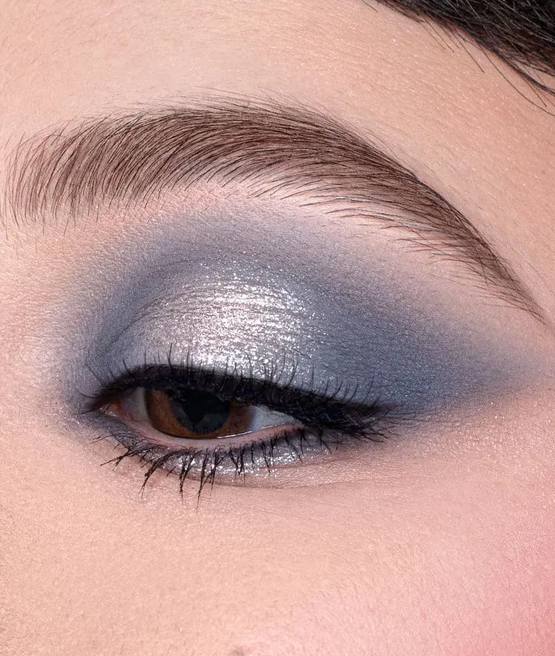 Close-up eye with metallic silver lid blended into a smoky blue-grey crease and winged liner