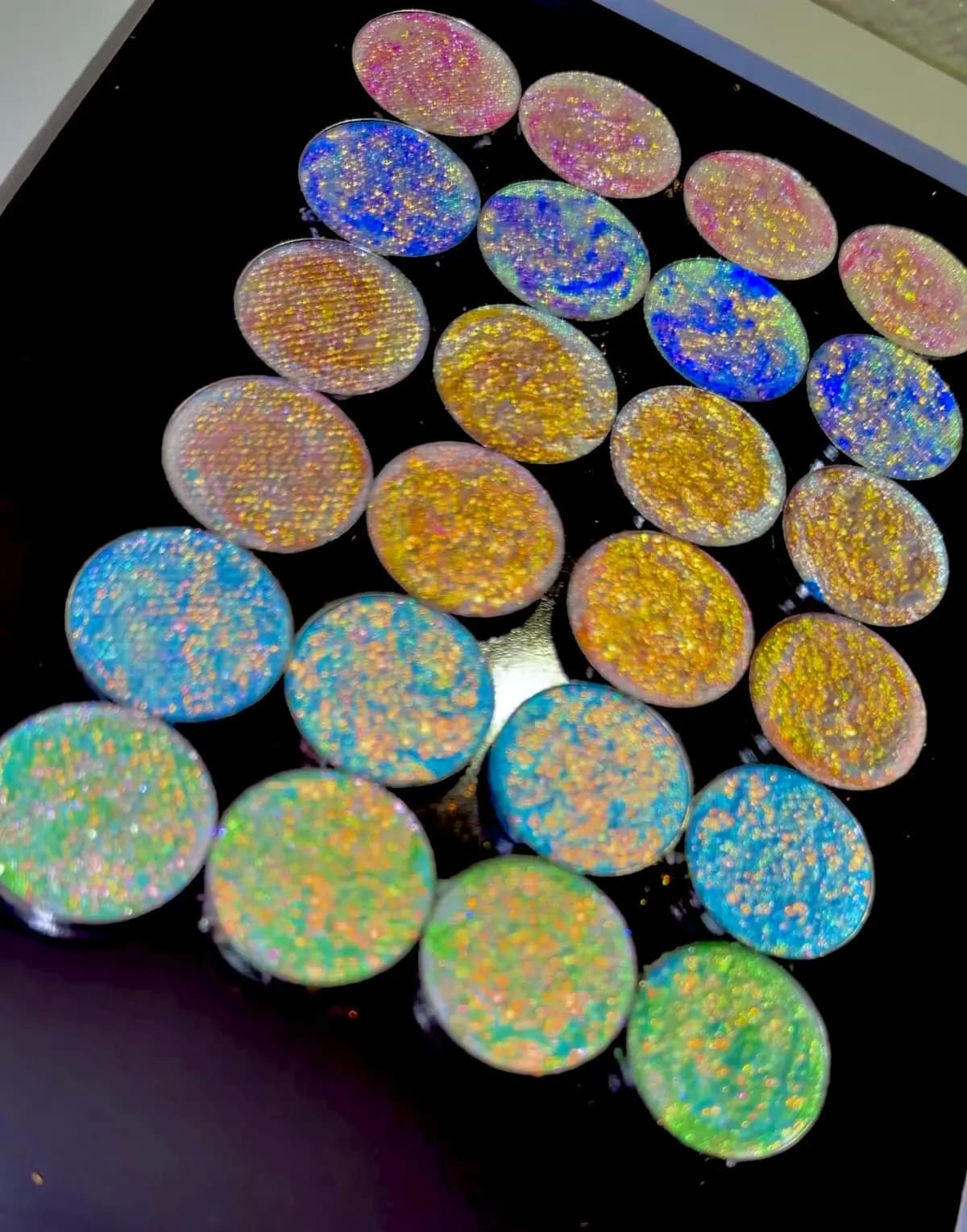 Rows of round multichrome eyeshadow pans in pink, blue, gold, aqua and green with glittery flecks
