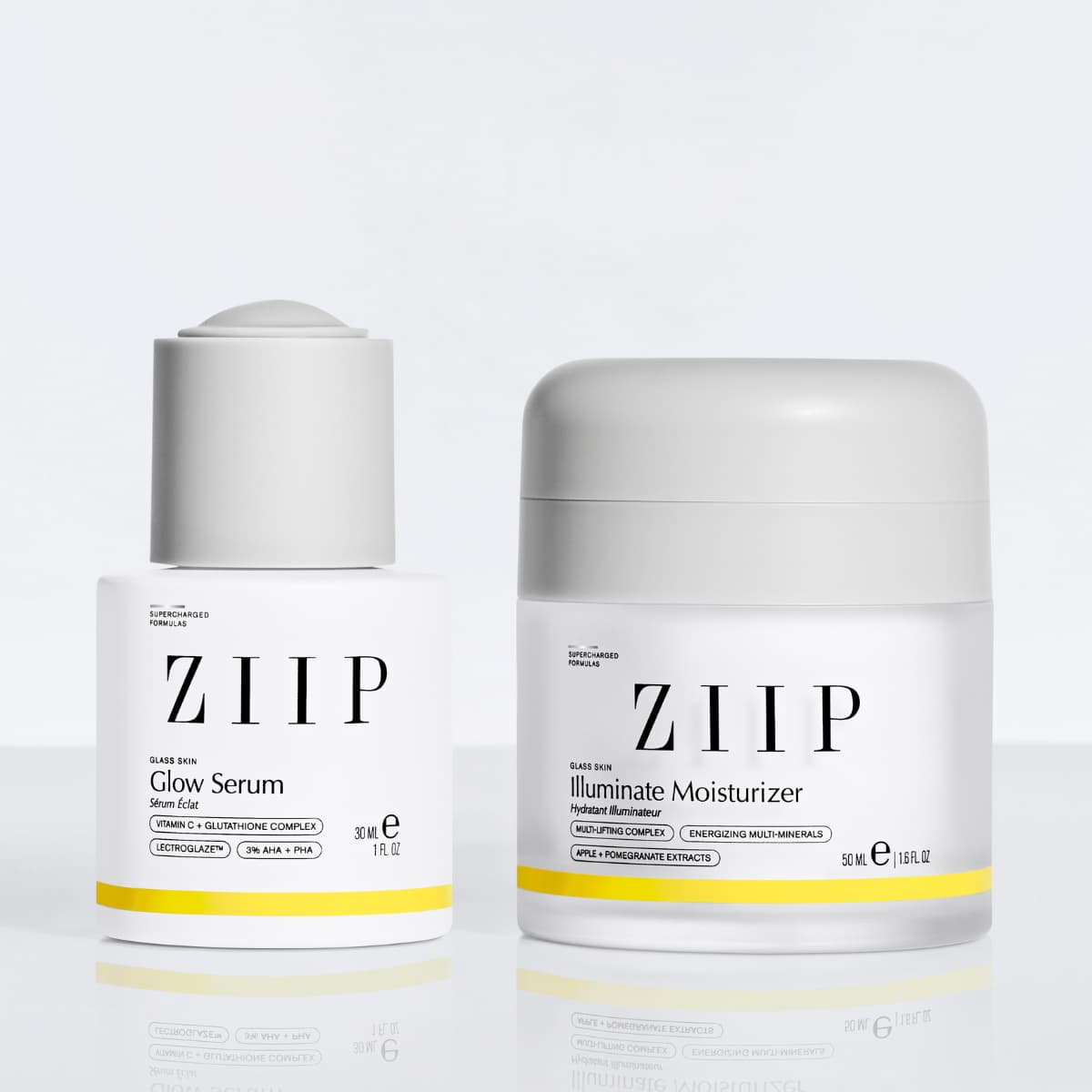Glow Serum and Illuminate Moisturizer side by side with grey caps on a reflective white surface