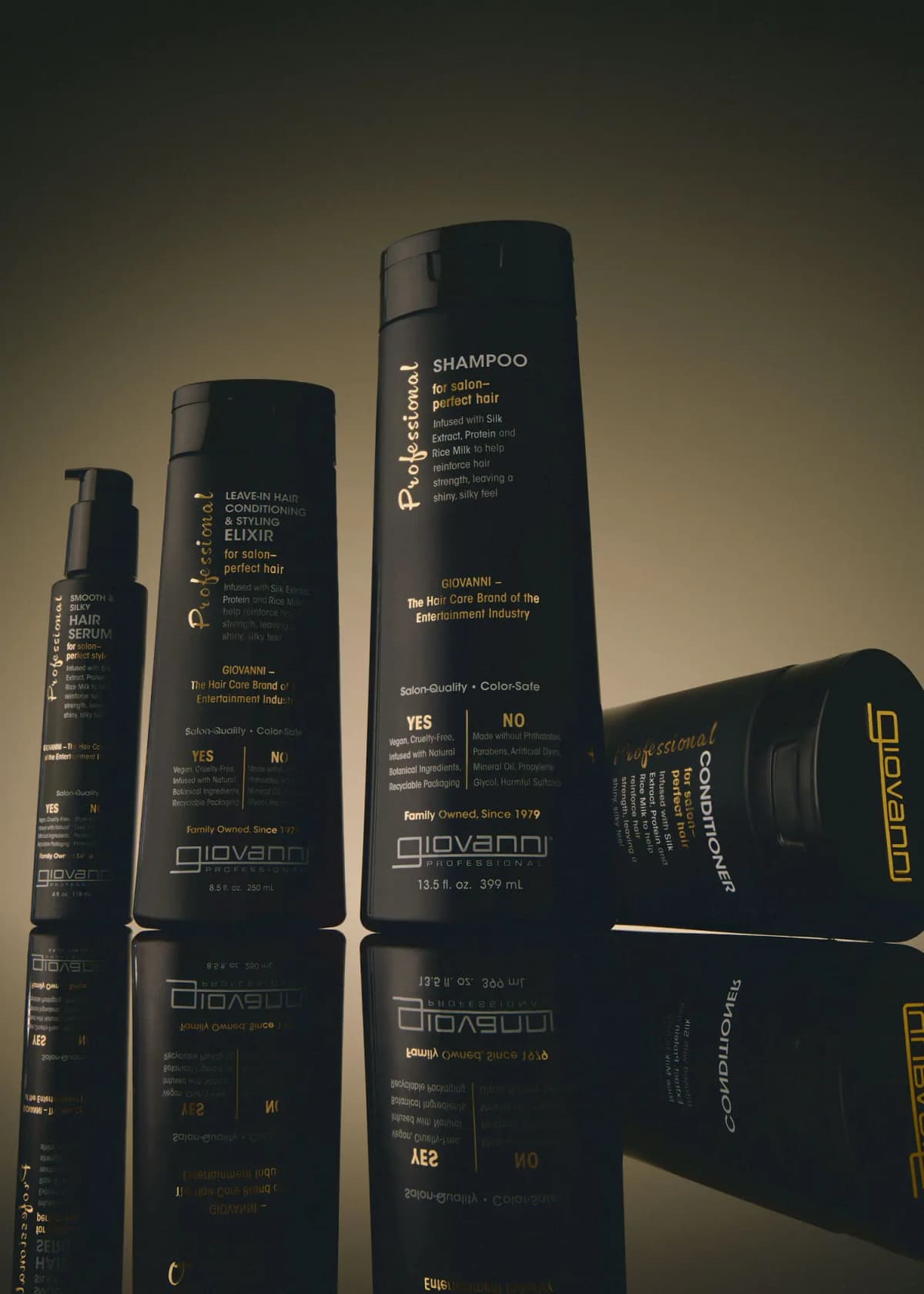 Giovanni Professional serum, elixir and shampoo standing upright beside a tipped conditioner on a reflective surface.