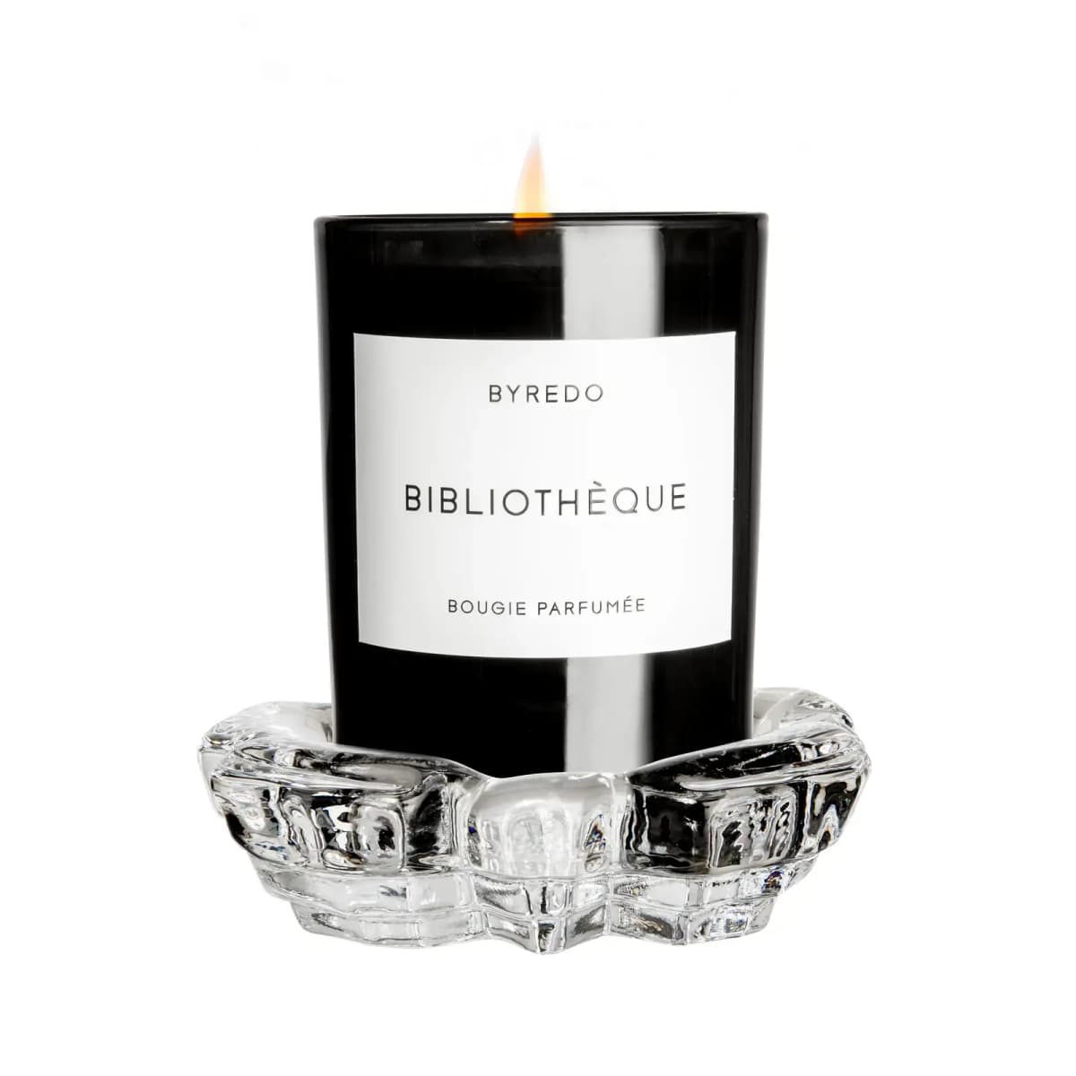 Lit black Byredo Bibliothèque candle resting in a chunky clear glass holder dish