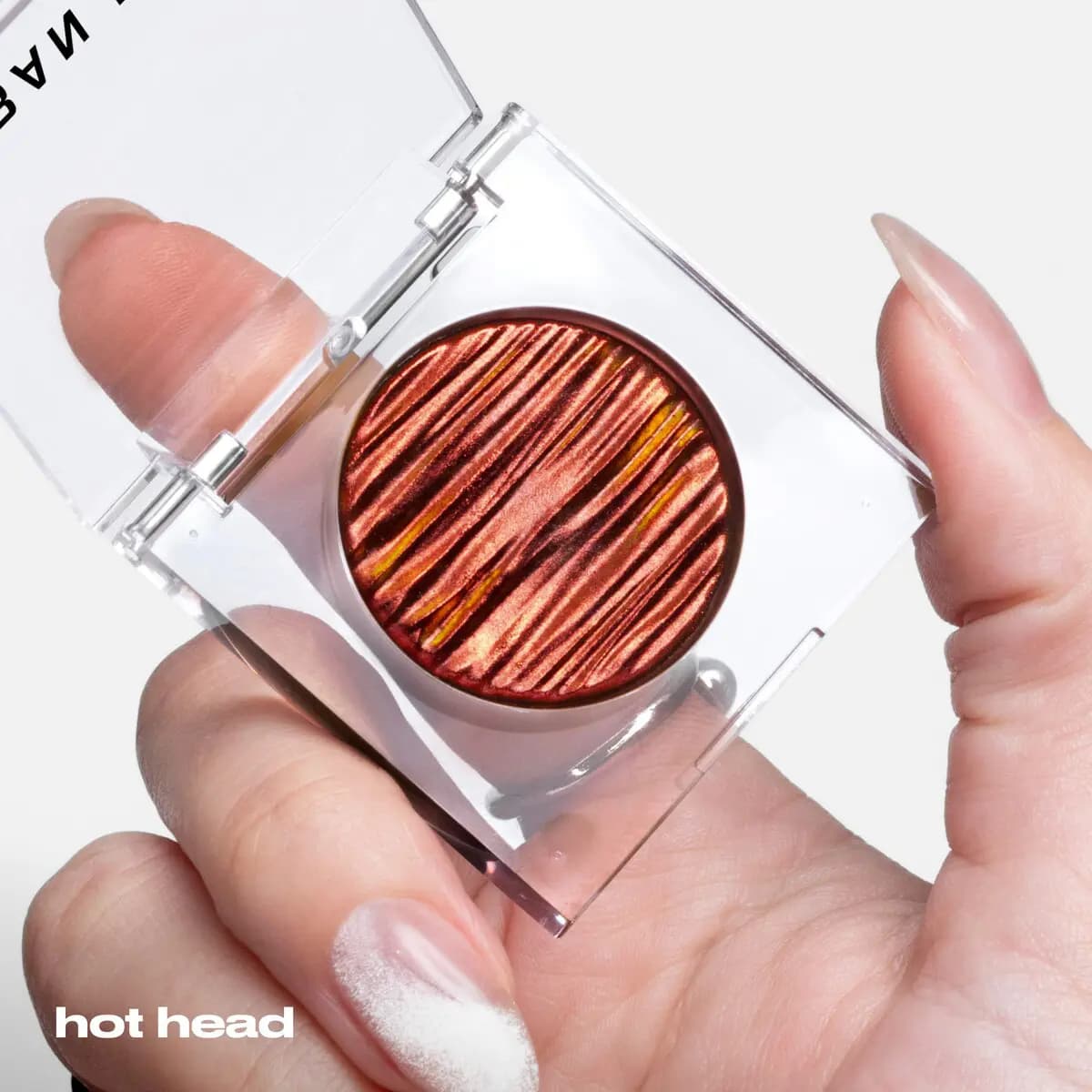 Hand with almond nails holding an open clear compact of Hot Head, its copper red ridges flashing gold.