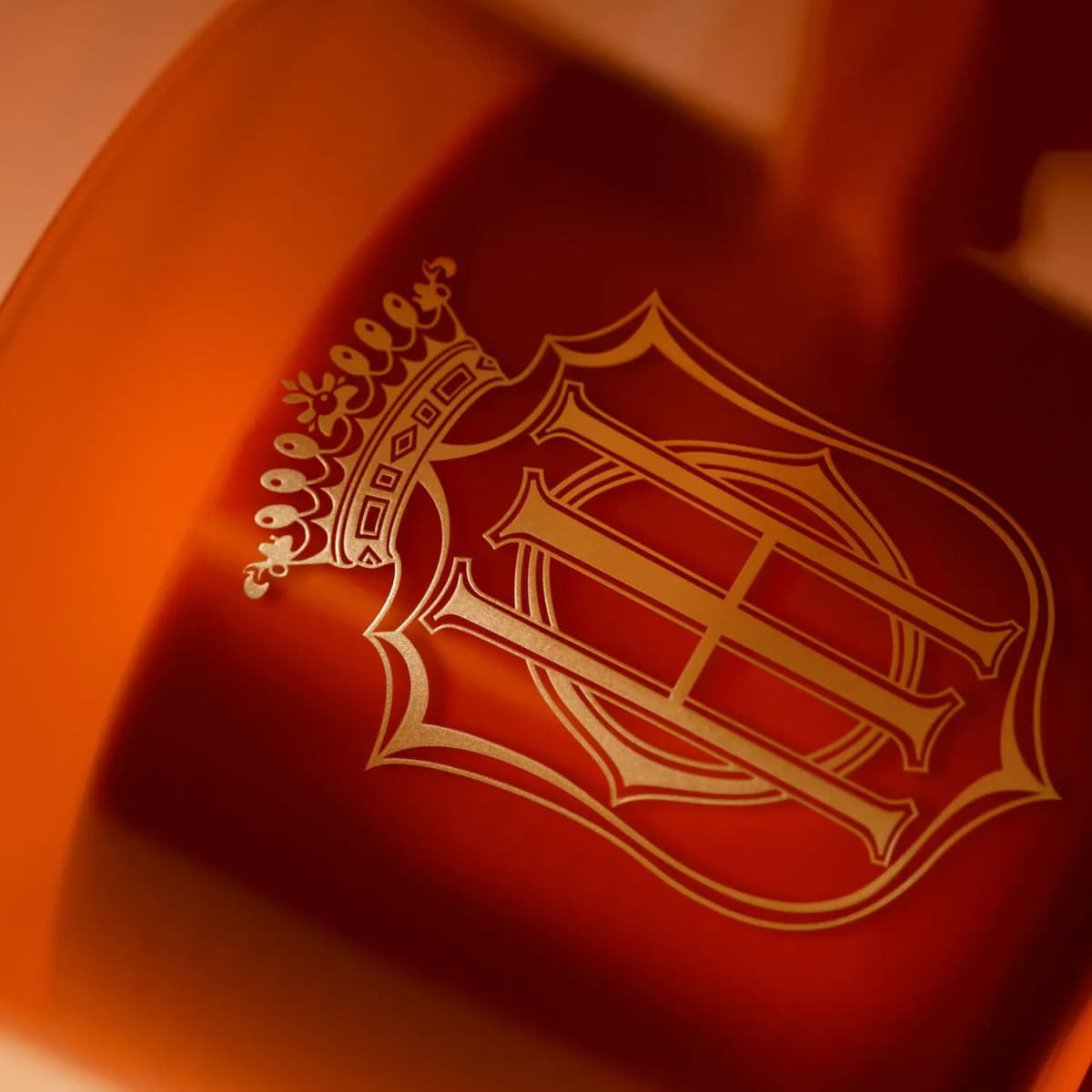 Close-up of the gold crowned shield monogram etched on deep orange glass