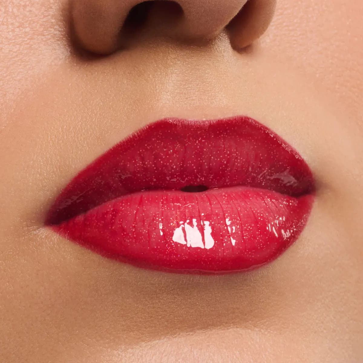 Close-up of full lips wearing a shimmery red glossy lip tint