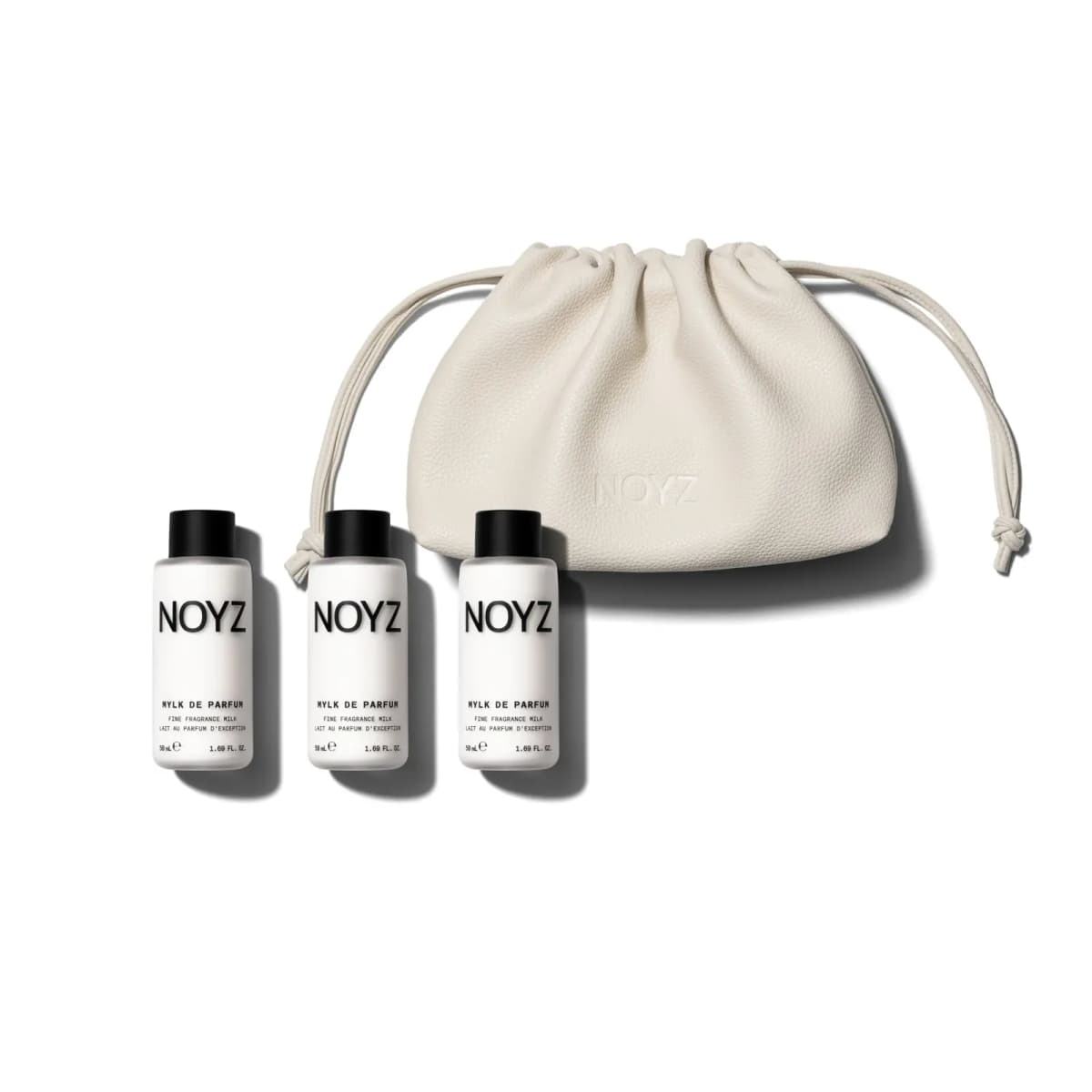 Three 50 mL Mylk de Parfum fragrance milks with black caps beside a cream pebbled drawstring pouch embossed NOYZ