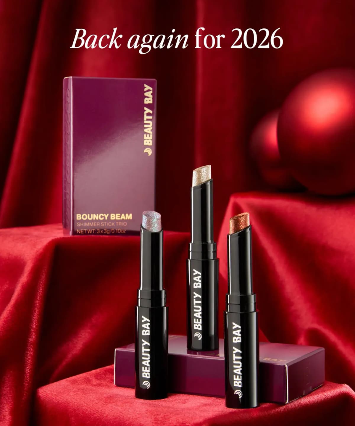 Three Bouncy Beam shimmer sticks posed on red velvet with box and red baubles, captioned 'Back again for 2026