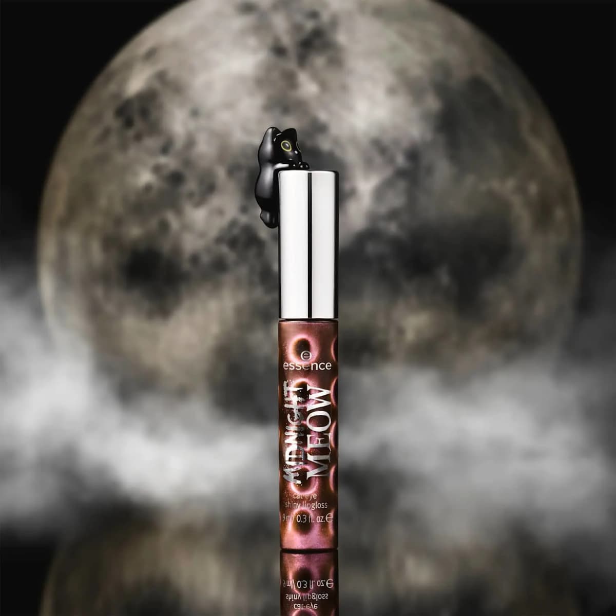 Closed lip gloss with cat-topped silver cap against a full moon and misty clouds, reflected on a glossy surface
