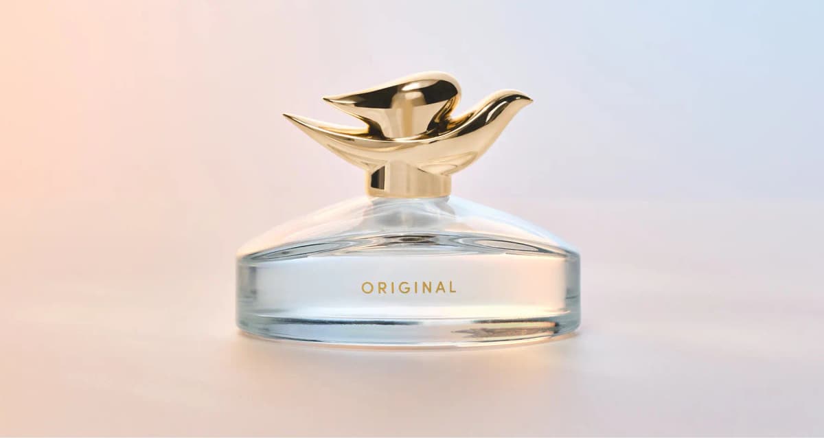 Dove Original Fragrance Eau de Parfum bottle with gold dove-shaped cap on a soft peach-to-lilac gradient background