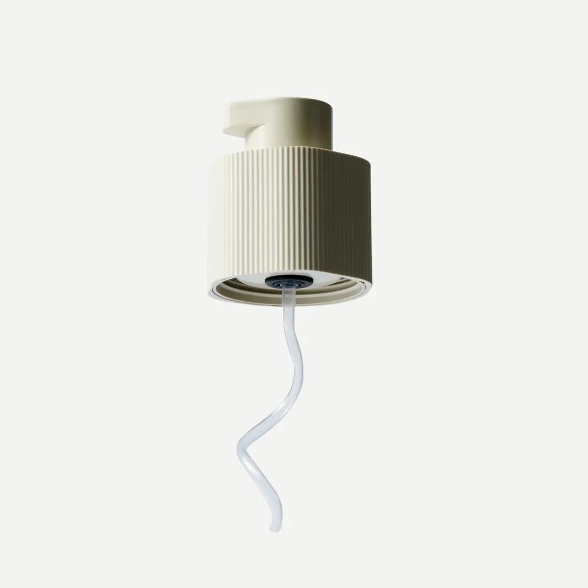Cream ribbed pump head detached from its capsule, showing a clear curly dip tube underneath