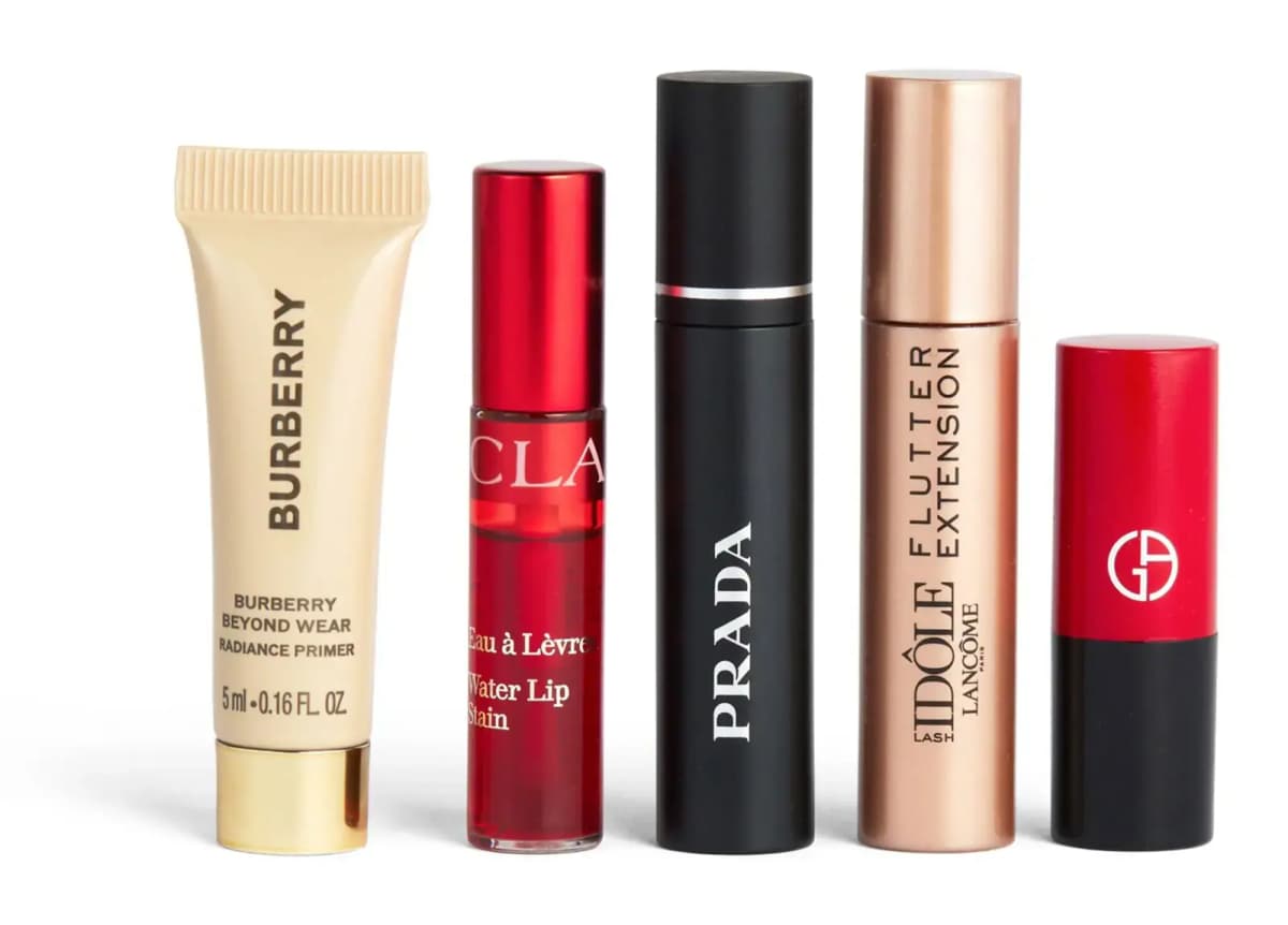 Five minis in a row: Burberry primer tube, red Clarins lip stain, black Prada and rose-gold Lancôme mascaras, Armani lipstick