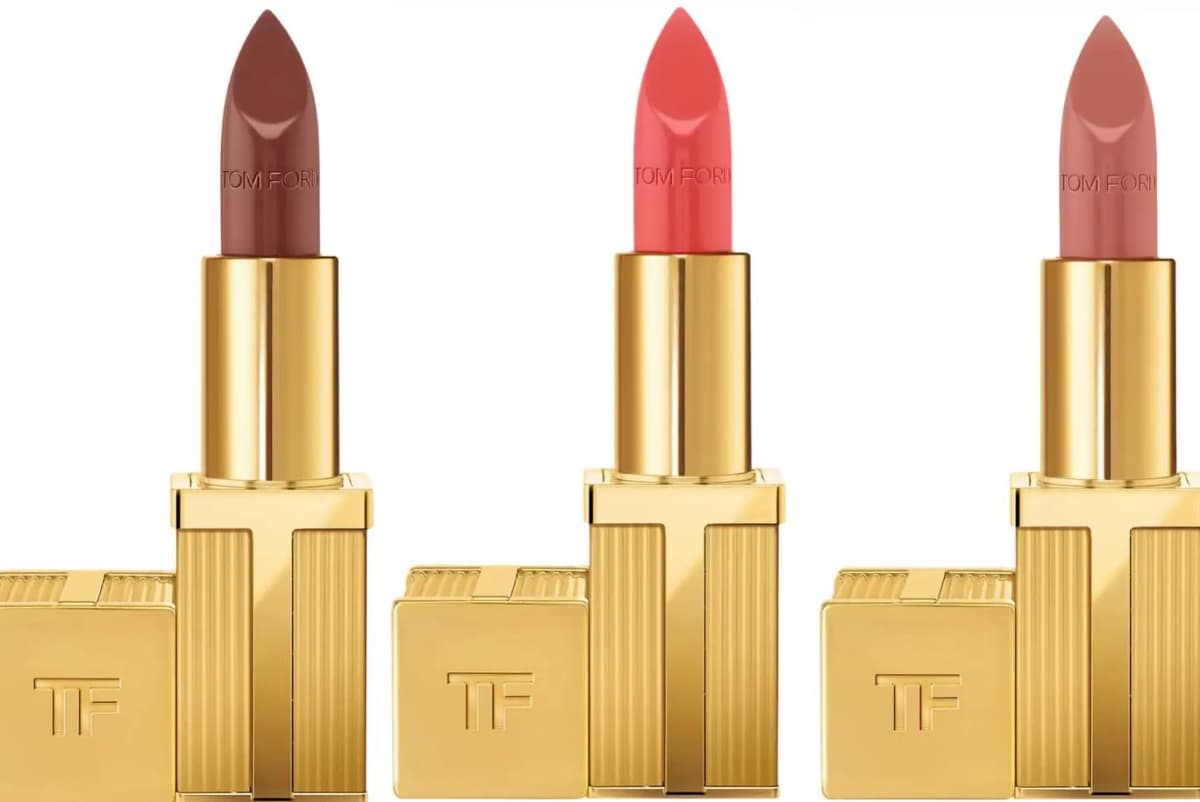 Three gold Tom Ford lipsticks in brown, coral and rosy nude, each with a TF cap, on a white background