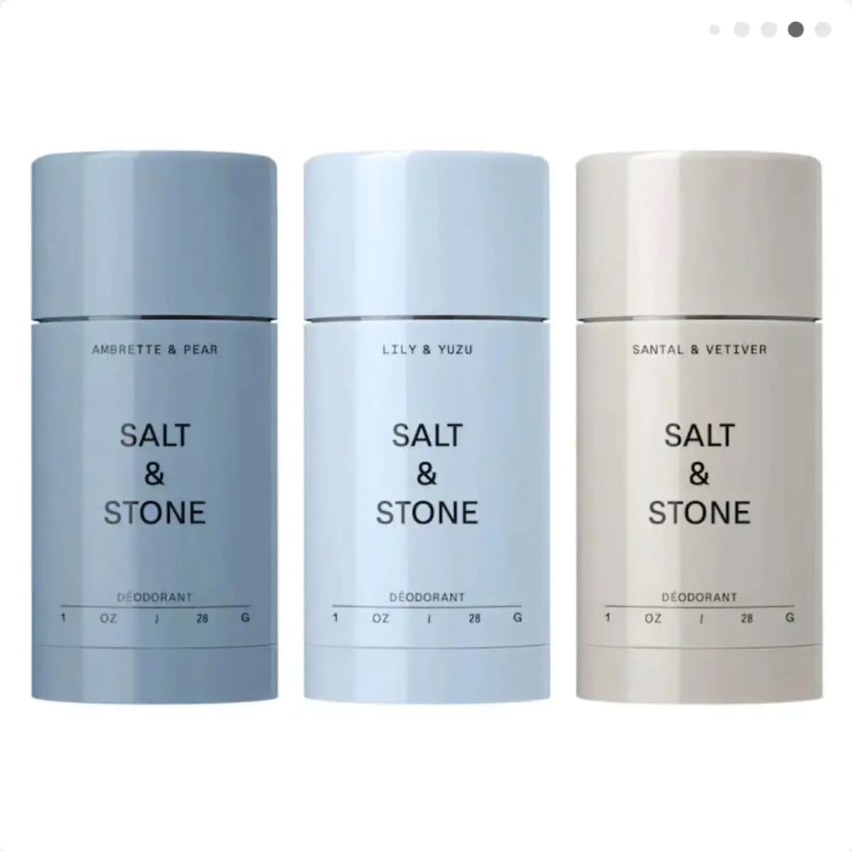 Three full-size Salt & Stone deodorant sticks lined up: Ambrette & Pear, Lily & Yuzu, and Santal & Vetiver in blue and cream.