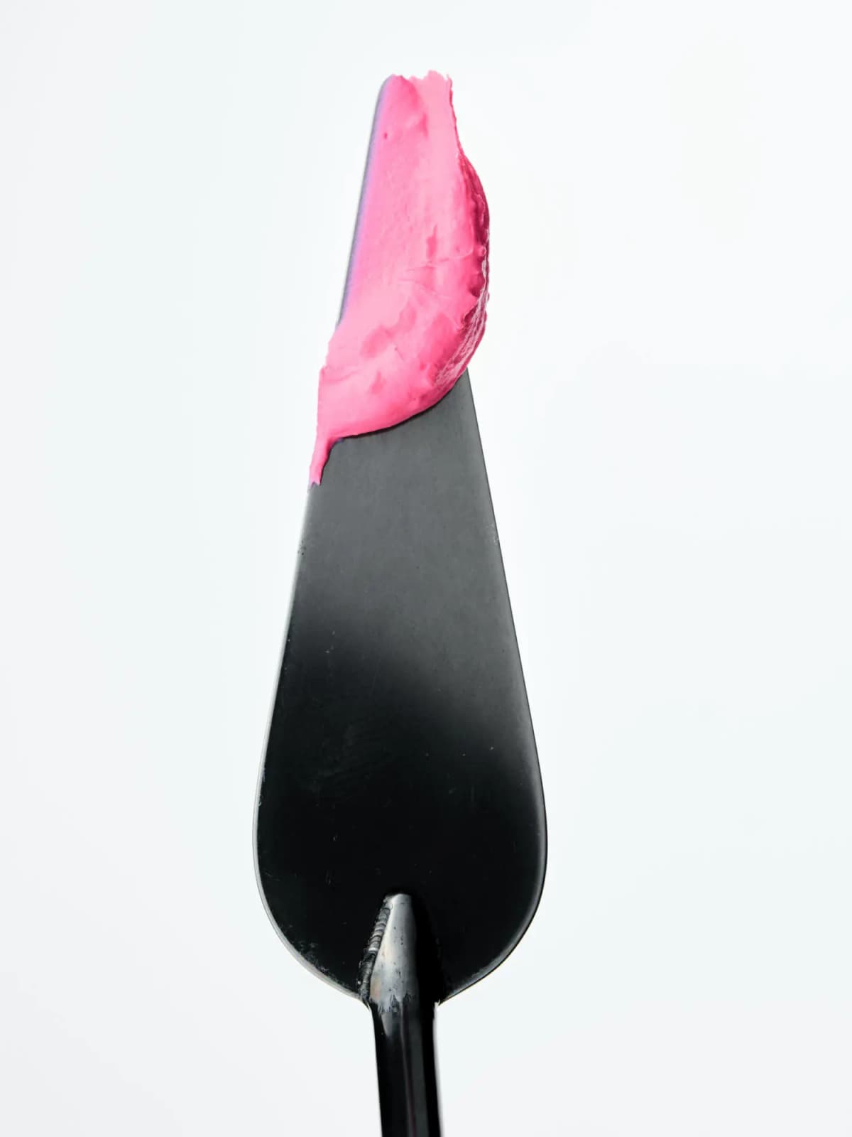 Swipe of whipped hot-pink mousse blush on the tip of a black metal spatula