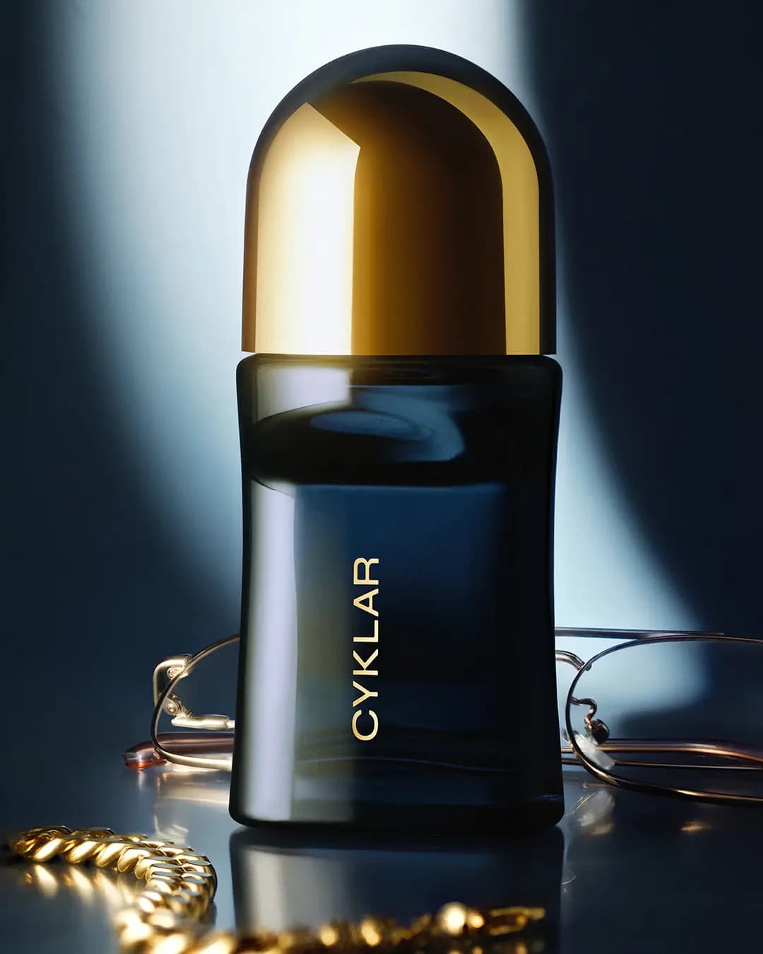 Deodorant roll-on in a cool blue spotlight beside wire-frame glasses and a gold chain