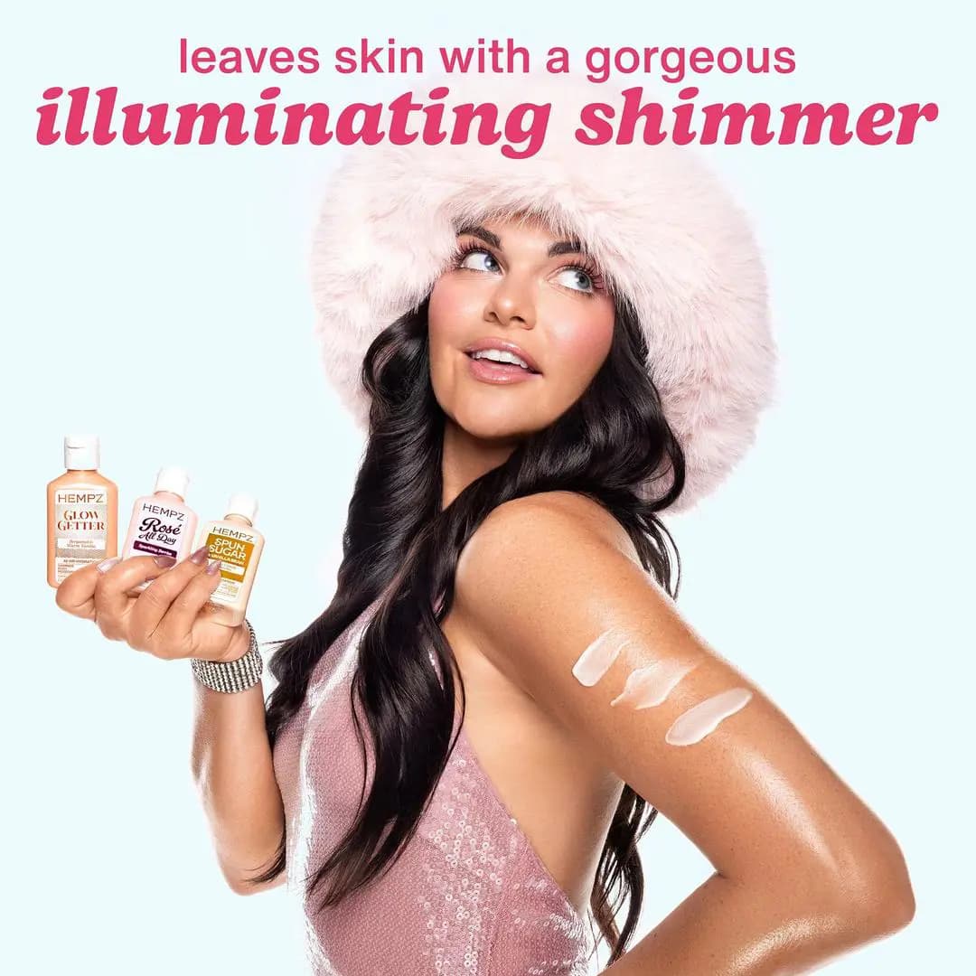 Brunette model in pink fur hat and sequin top holding three shimmer lotions with glistening swatches on her arm