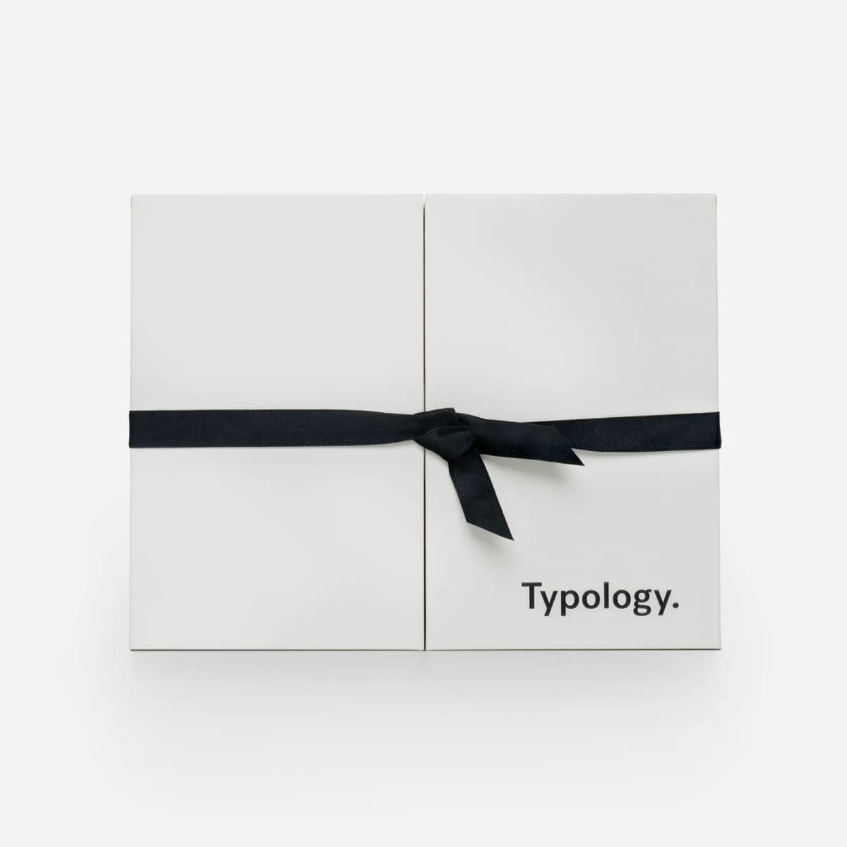 Closed white Typology Advent Calendar box tied with a black satin ribbon bow, brand name printed in black at bottom right.