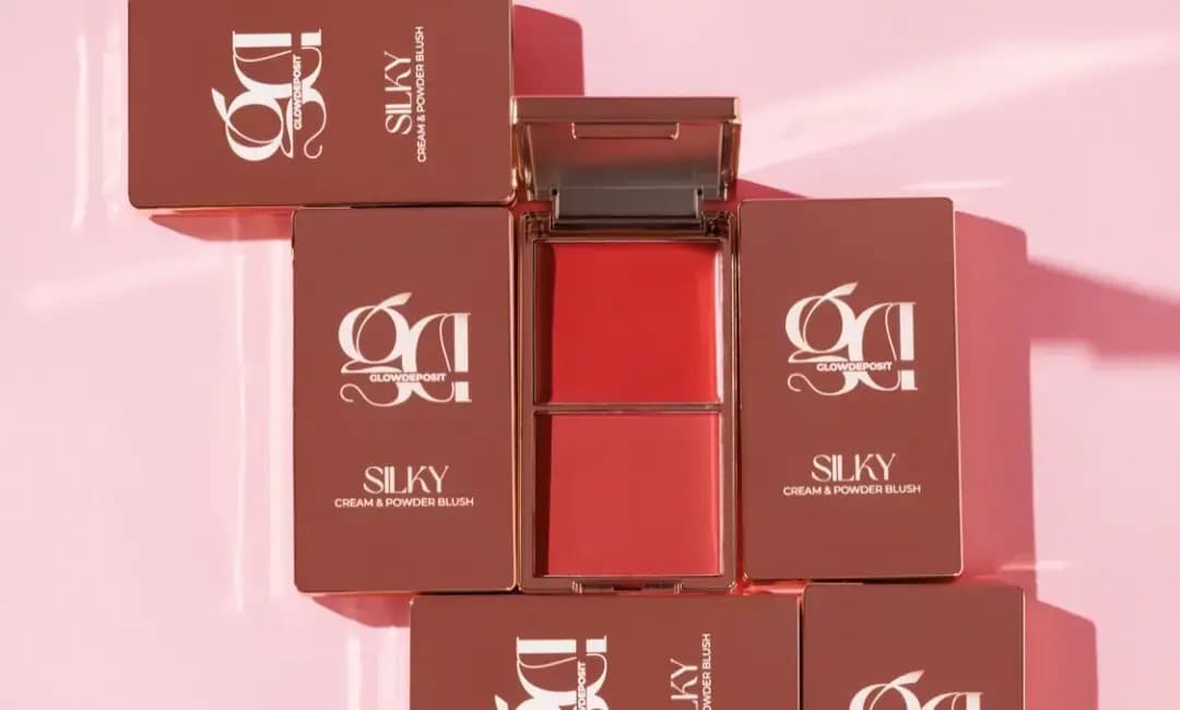 Open red-coral Silky blush duo surrounded by rose-brown Silky Cream & Powder Blush boxes on a glossy pink surface