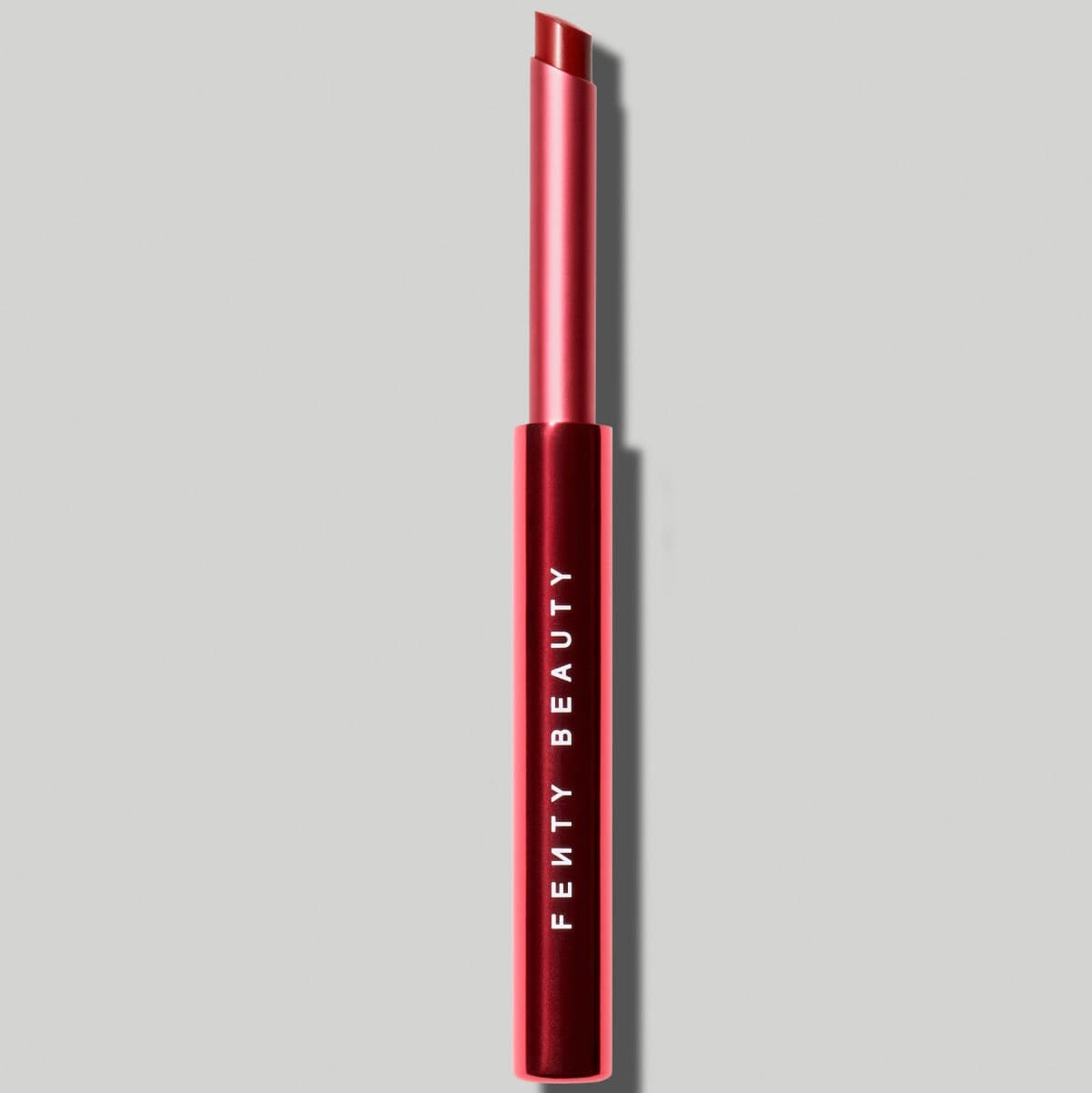 Slim red-to-pink tube with an angled deep red bullet, shown uncapped against a plain light grey background