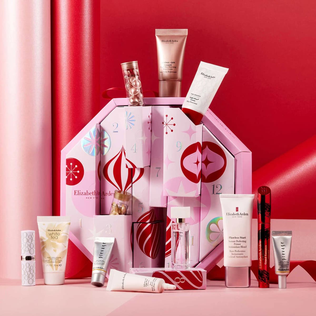 Opened pink ornament-print calendar with tubes and capsules popping out, Flawless Start primer and Grand Entrance Mascara.
