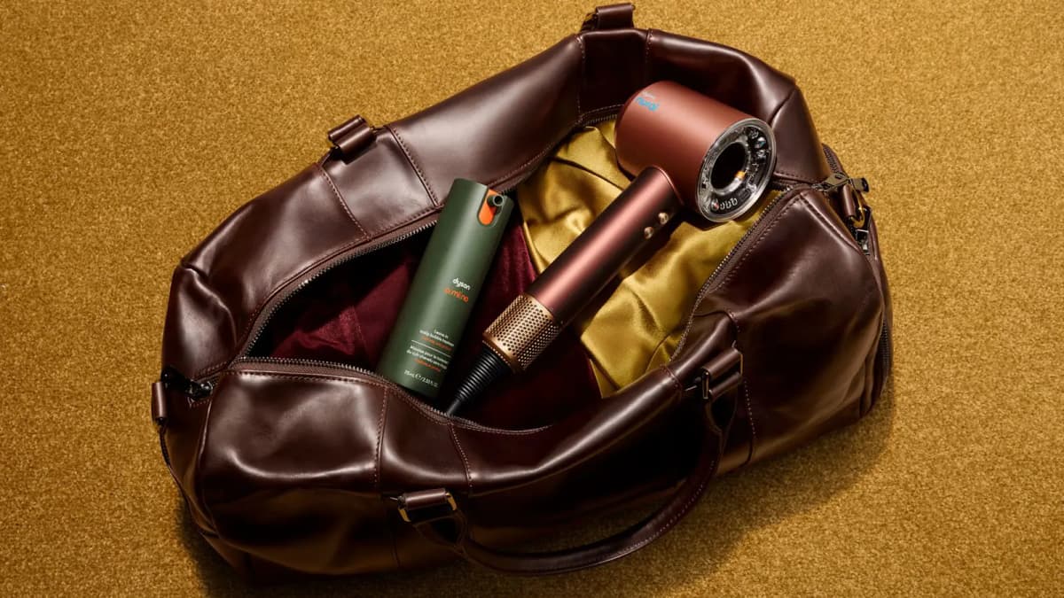Dyson Supersonic Nural dryer in copper with brass vent tucked in a leather duffel beside a green Dyson scalp treatment