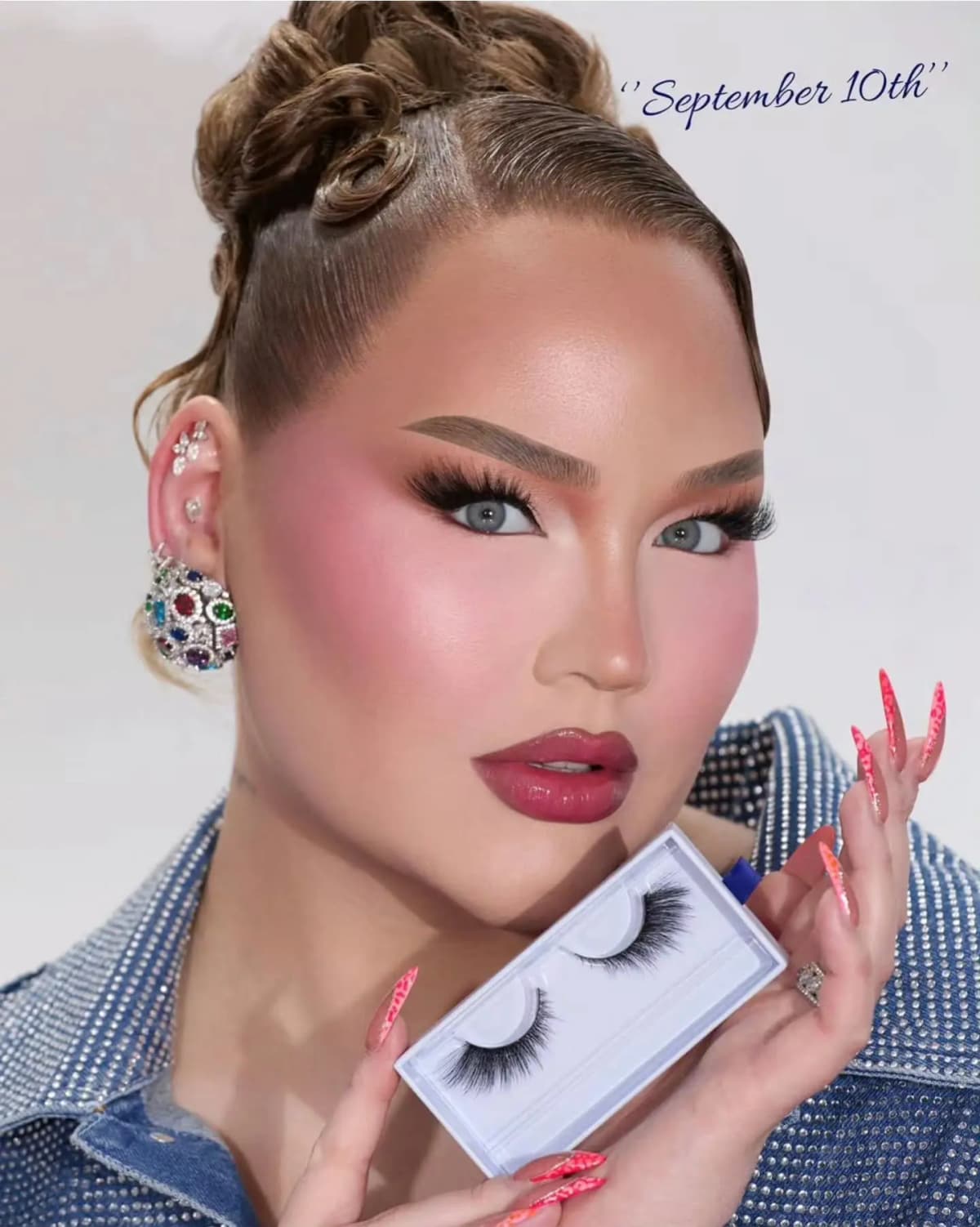 NikkieTutorials with pink blush and berry lips holds a boxed pair of lashes, marked 'September 10th' in the corner.