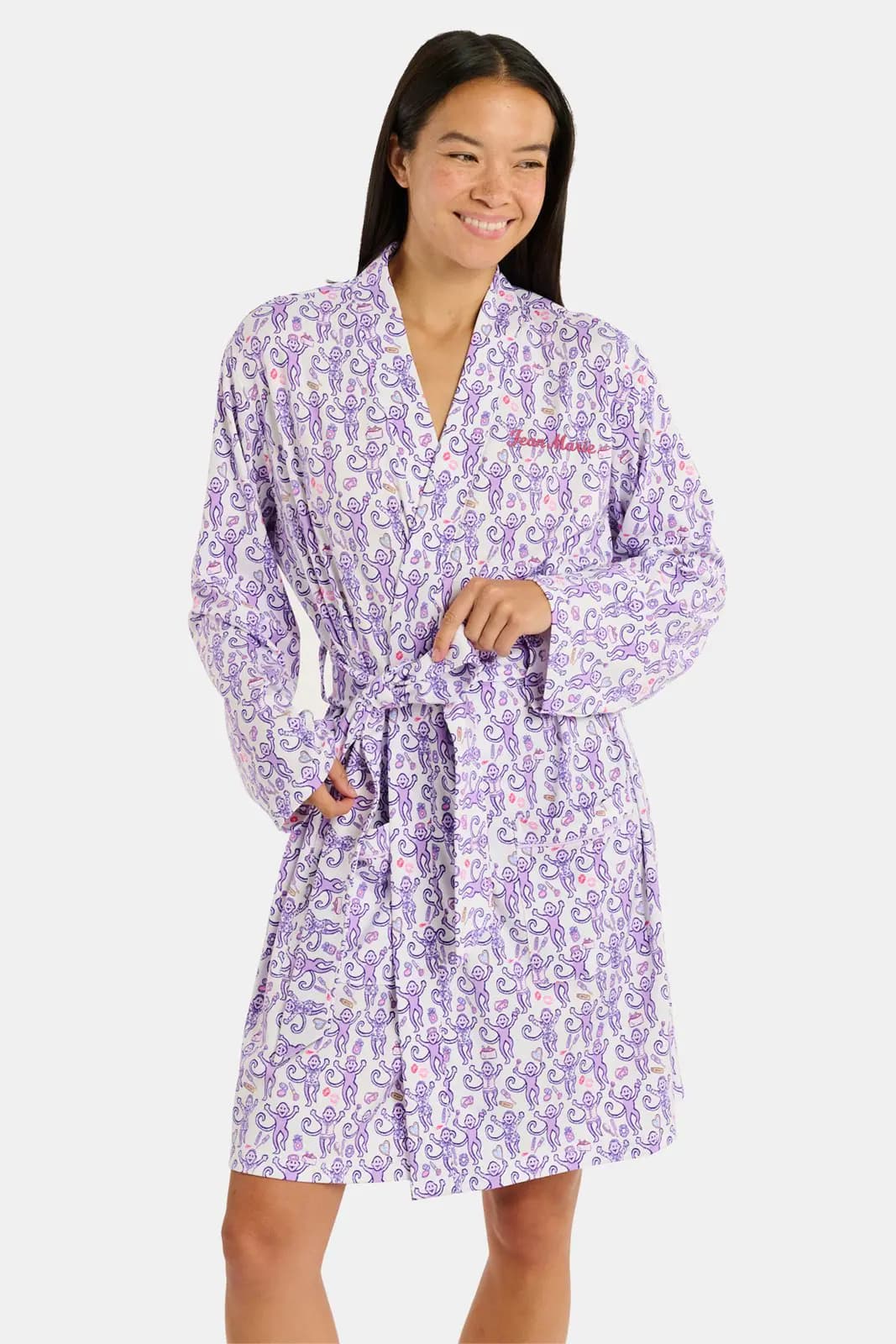 Smiling model tying a white and lavender monkey-print robe with pink embroidered name on chest