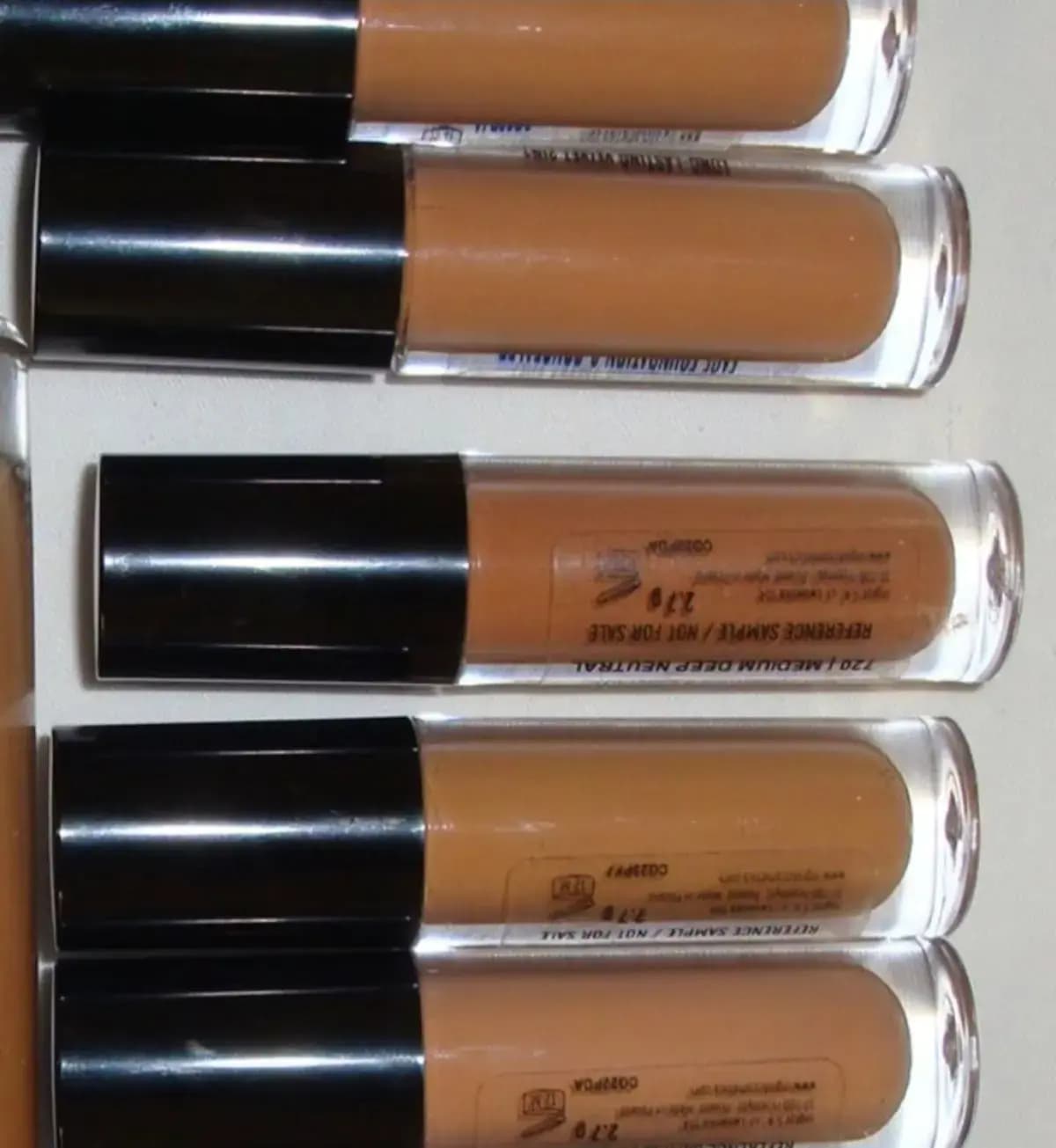 Mini tan-coloured sample vials, one labelled 720 Medium Deep Neutral, lying on a white surface