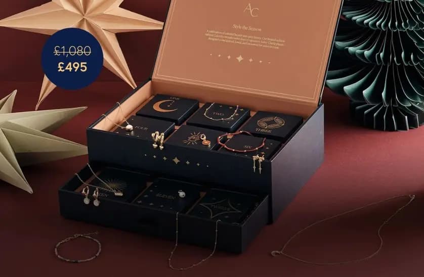 Open navy Astley Clarke advent calendar box with 12 numbered compartments displaying gold jewellery, priced £495 from £1,080