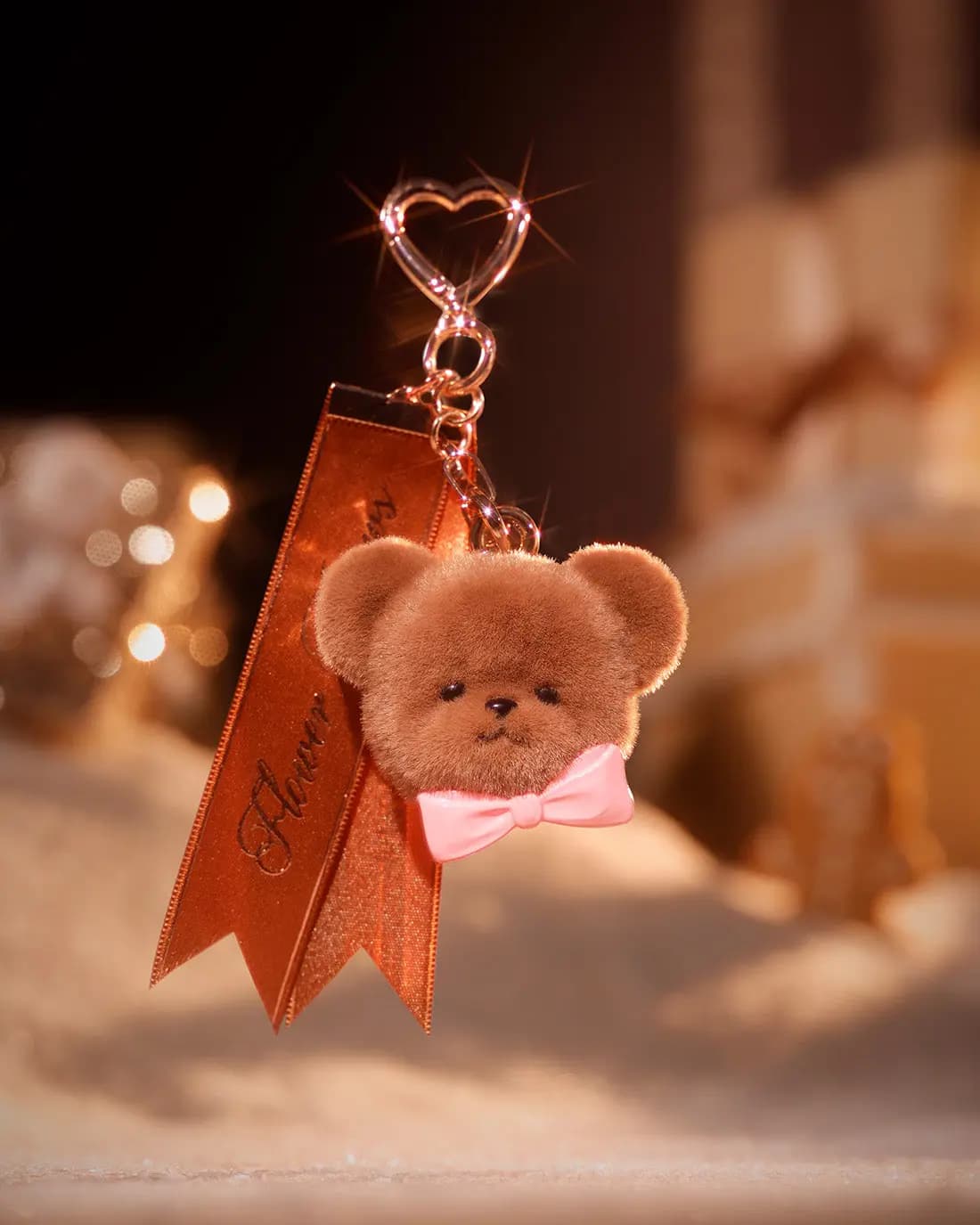 Fuzzy brown bear-head charm with pink bow tie on a heart clasp and copper Flower Knows ribbon