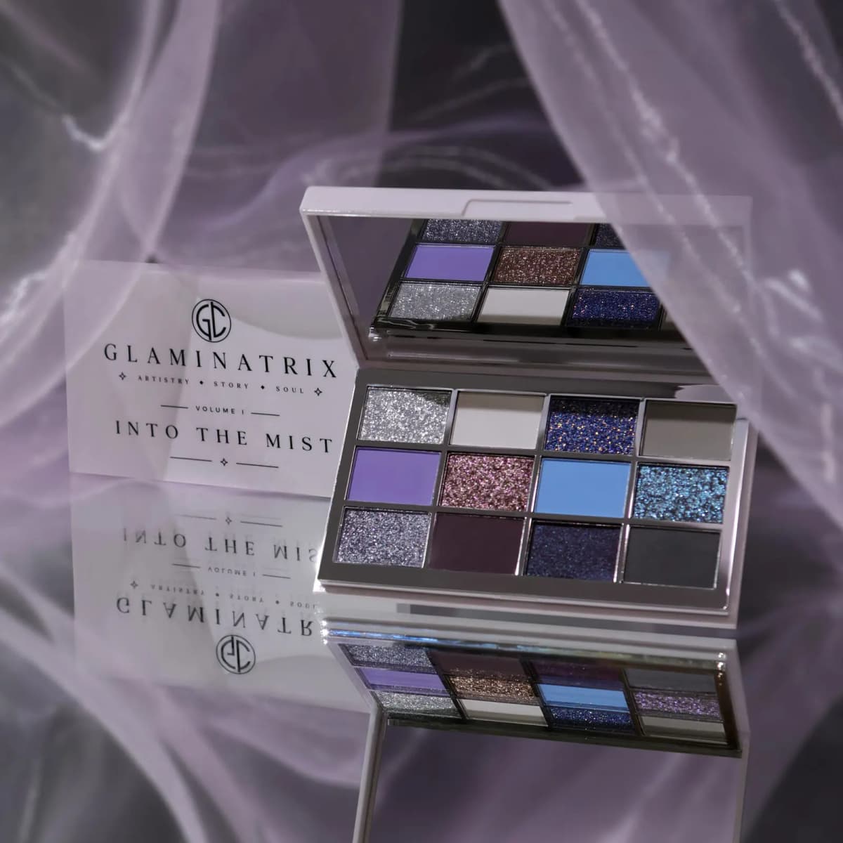 Open Into the Mist palette reflected in a mirrored surface with sheer lilac fabric draped around it.