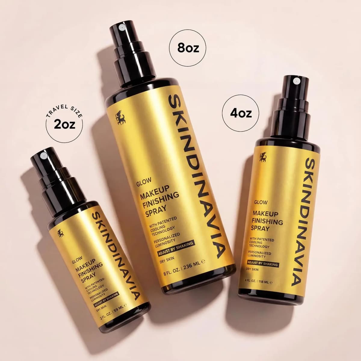 Gold Glow Makeup Finishing Spray in 2 oz, 8 oz and 4 oz bottles laid flat on a pale pink surface