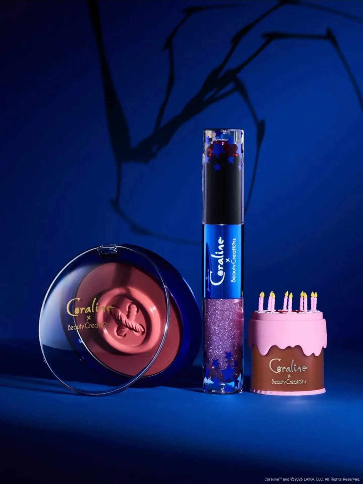 Button-shaped cream blush compact, dual-ended lip stain and gloss with star confetti, and pink birthday cake pot on blue