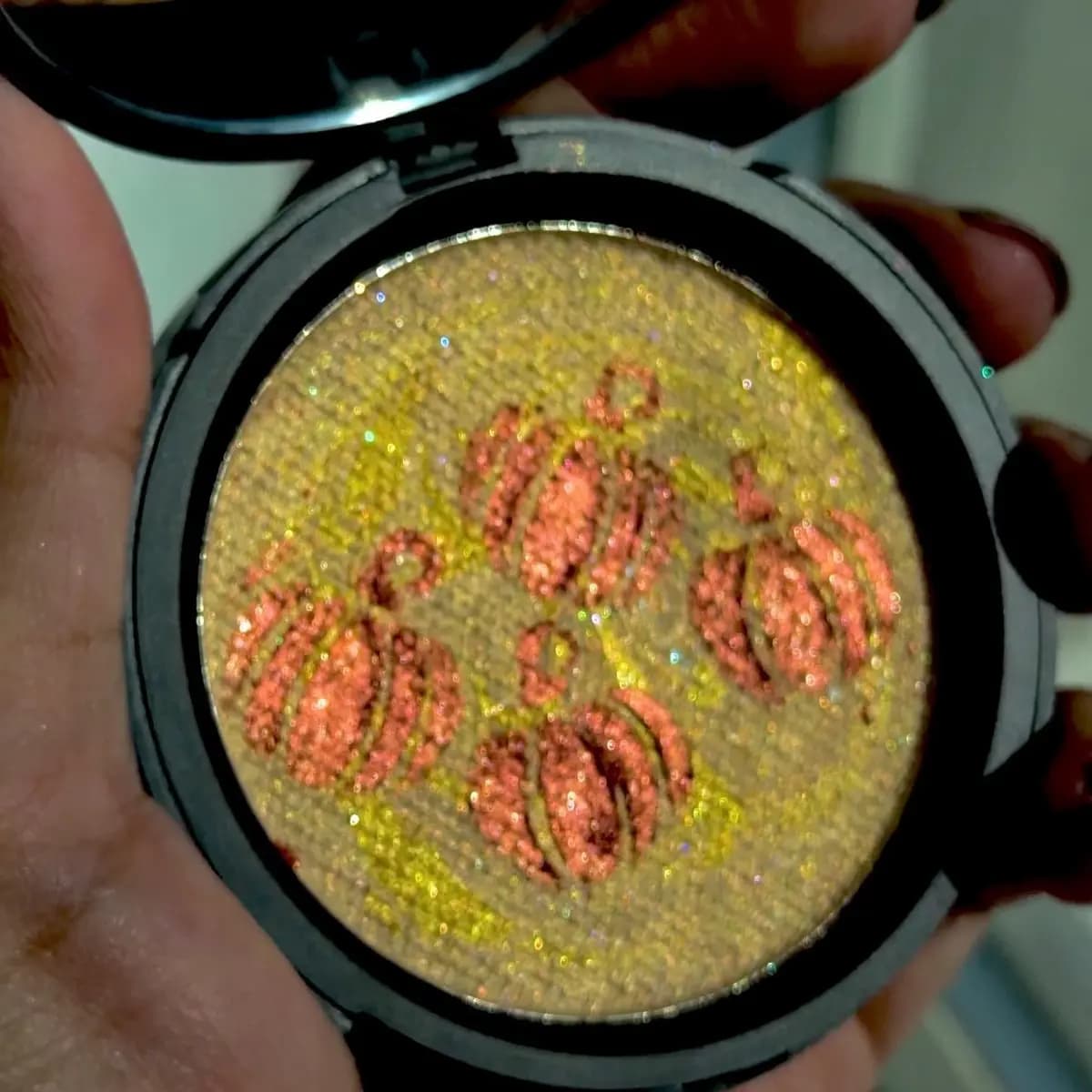Open compact showing gold multichrome highlighter embossed with four coppery-orange pumpkins