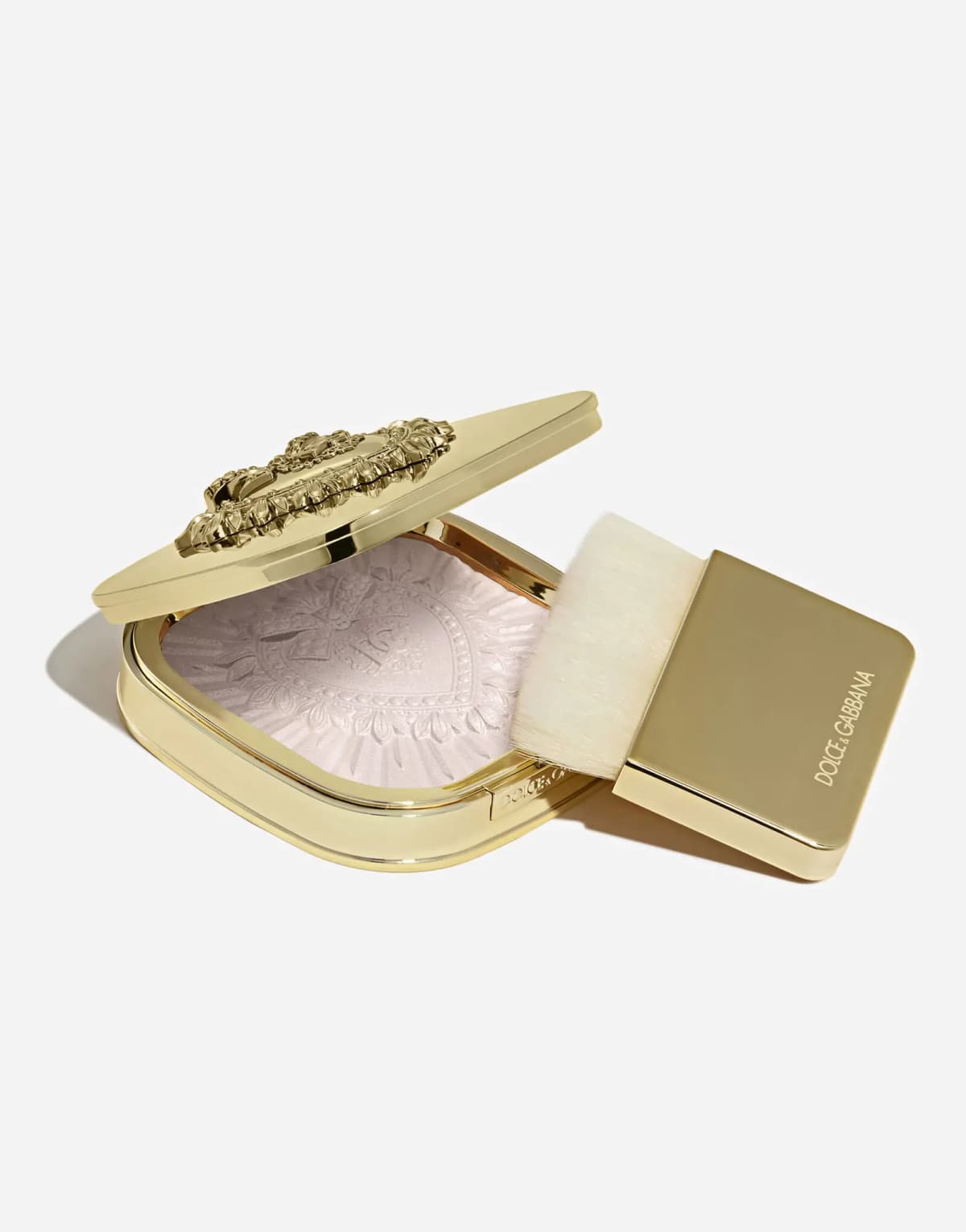 Tilted open compact with lilac-pink highlighter next to a gold flat brush with cream bristles