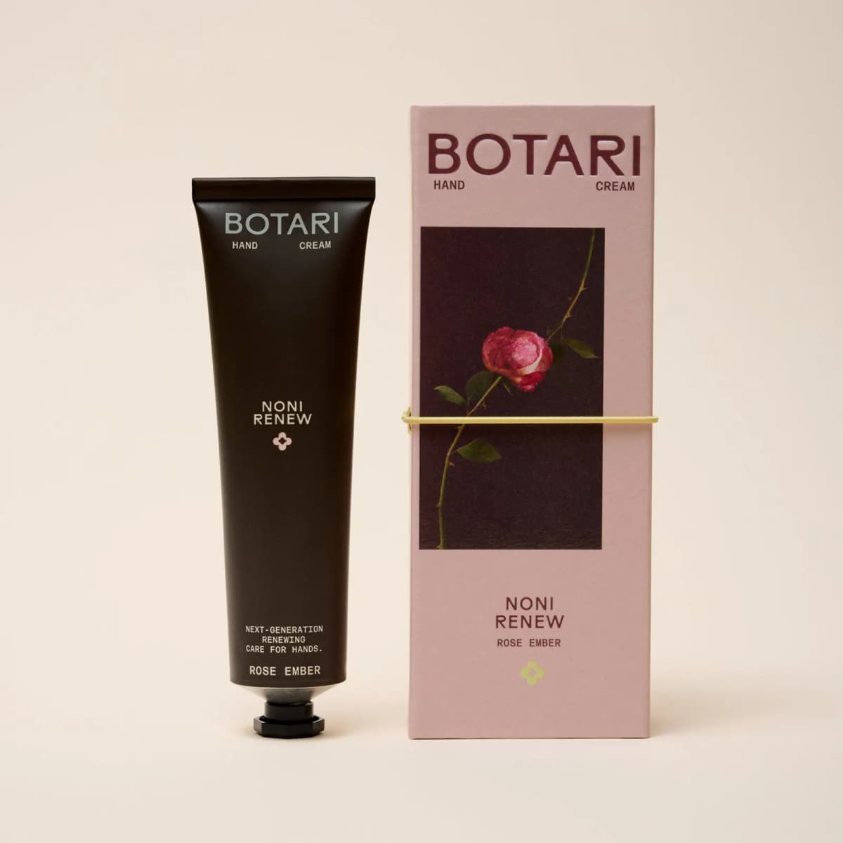 Dark brown BOTARI Noni Renew Rose Ember tube beside its pink box featuring a pink rose on a thorny stem