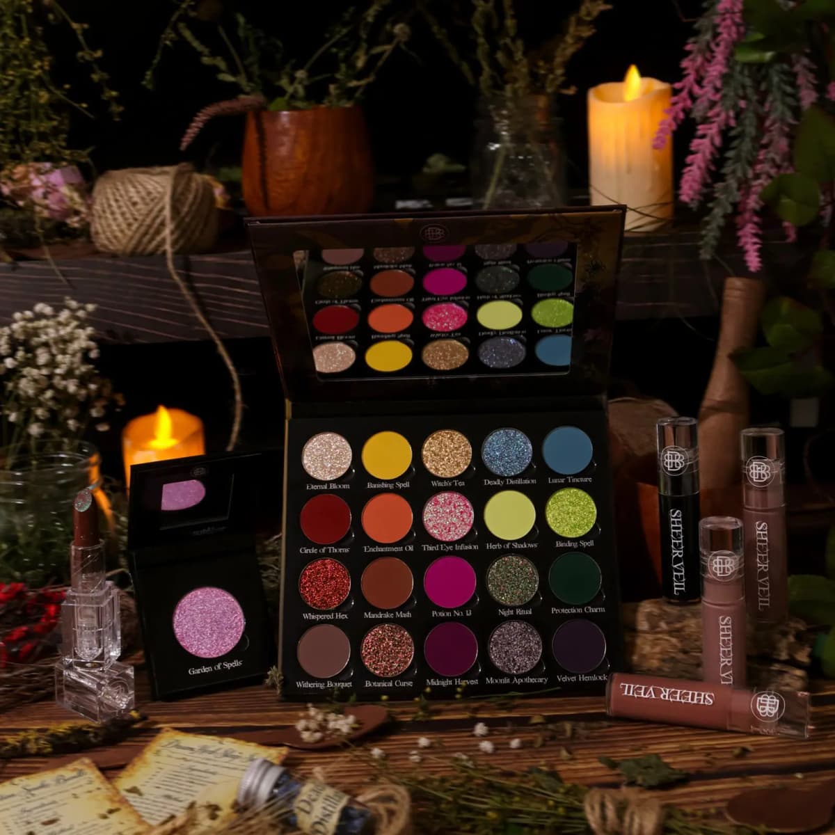 Garden of Spells 20-pan eyeshadow palette with single shadow, lipstick and Sheer Veil glosses among candles and herbs